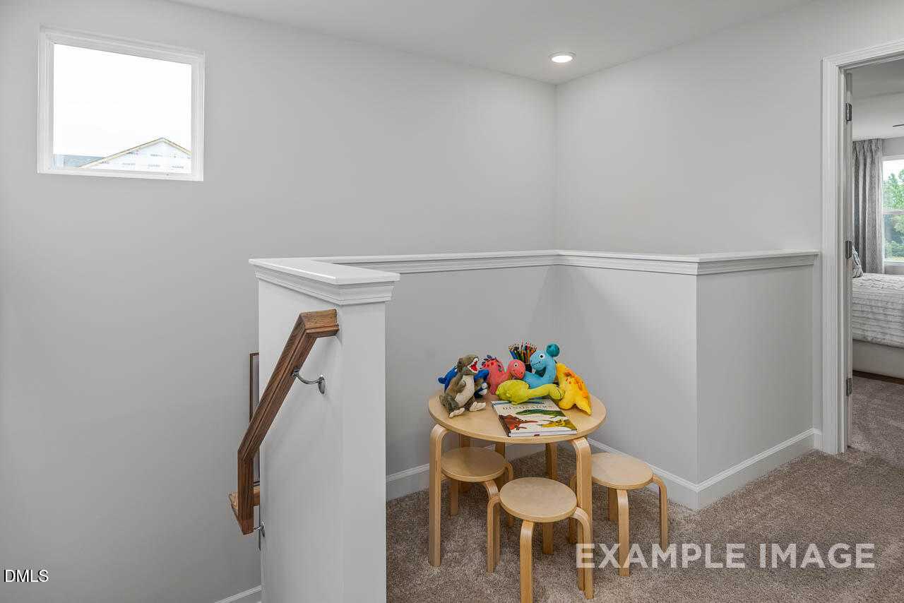 Cozy upstairs loft with kids' wooden table, stuffed toys, and chairs overlooking stairs in Davidson Homes The Graham, Fuquay-Varina, NC
