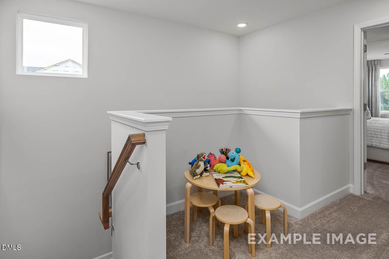 Cozy upstairs loft play area with wooden kids' table, colorful stuffed toys, and stools overlooking staircase in Davidson Homes The Graham, Fuquay-Varina