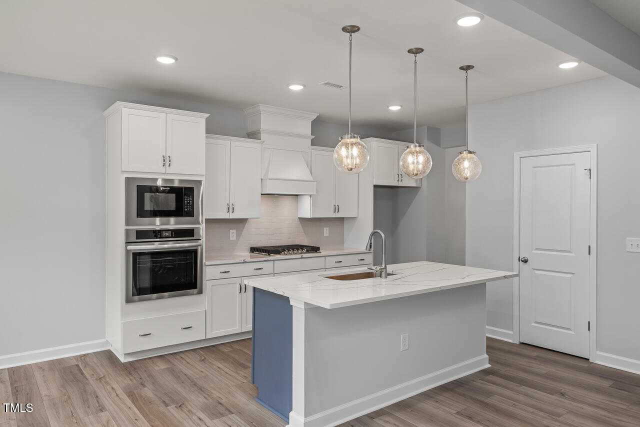 Modern white kitchen with shaker cabinets, double ovens, gas cooktop, and island sink in Davidson Homes The Willow G, Wake Forest, NC