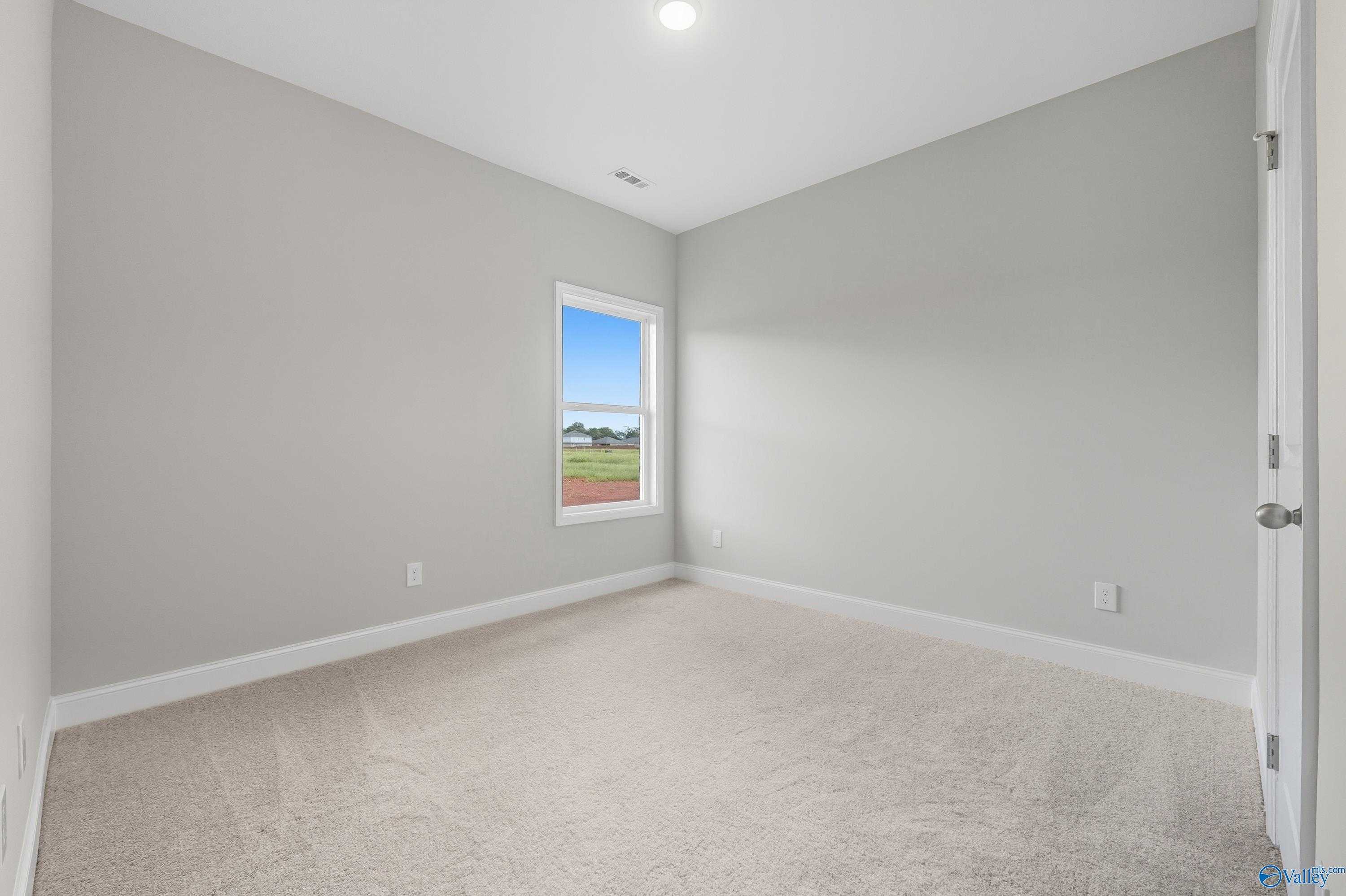 Bright secondary bedroom with light gray walls, beige carpet, and window view in Davidson Homes The Franklin, Meridianville, Alabama