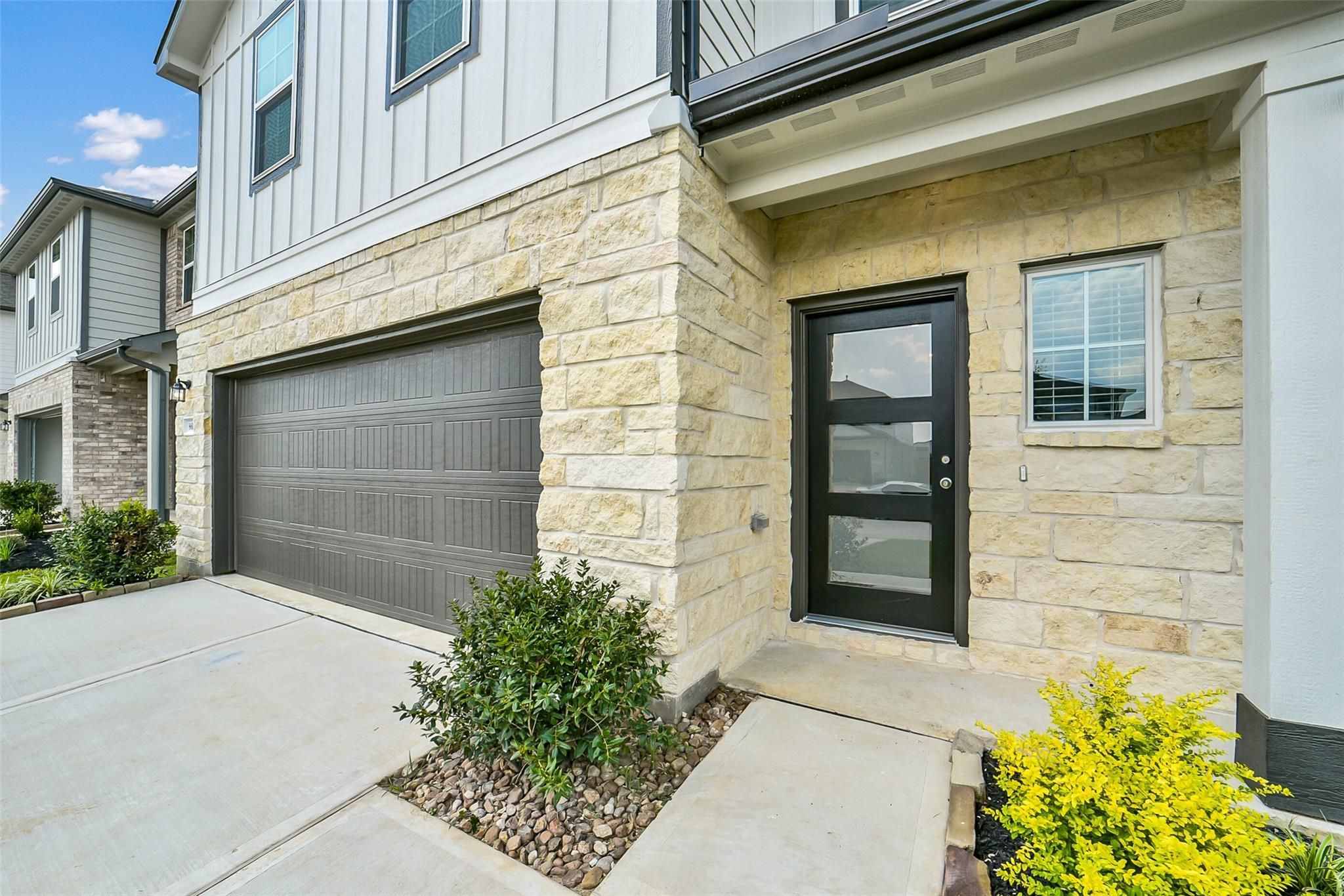Modern two-story home front with beige stone accents, 2-car garage, glass door, and landscaped driveway in Davidson Homes The Blanco E, Magnolia, Texas