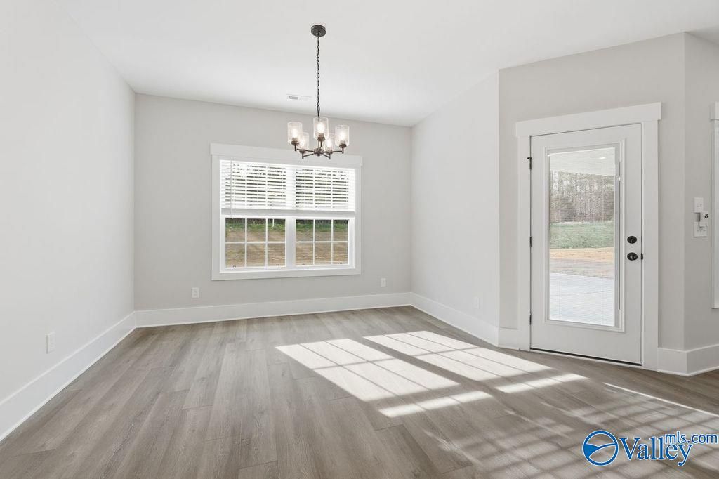 Bright dining room with chandelier, large window shutters, and glass door to wooded yard in Davidson Homes The Rockford, Hartselle, AL