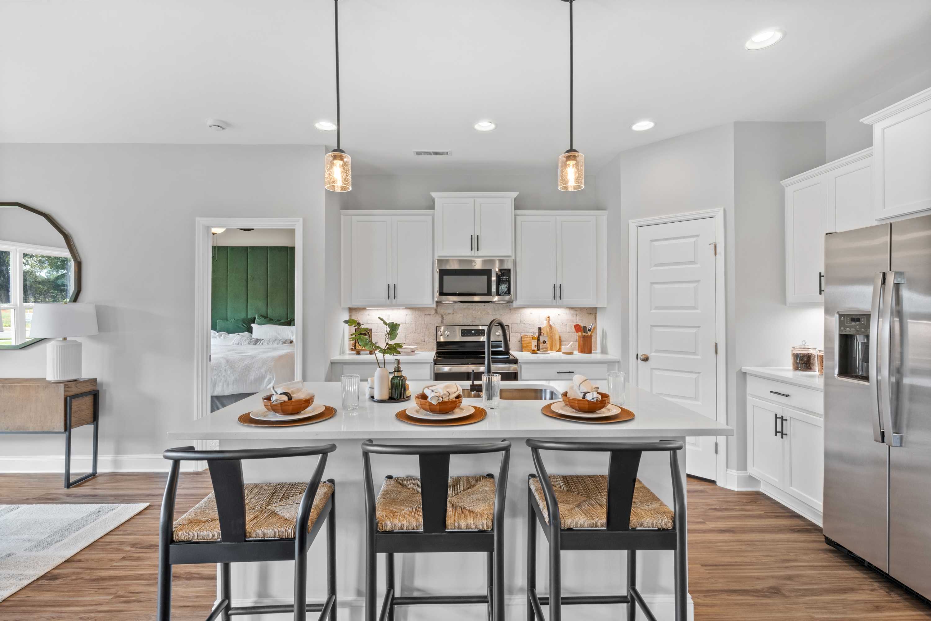Bright modern kitchen in Wood Trail, Toney Alabama with white cabinets, large island, pendant lights and hardwood floors