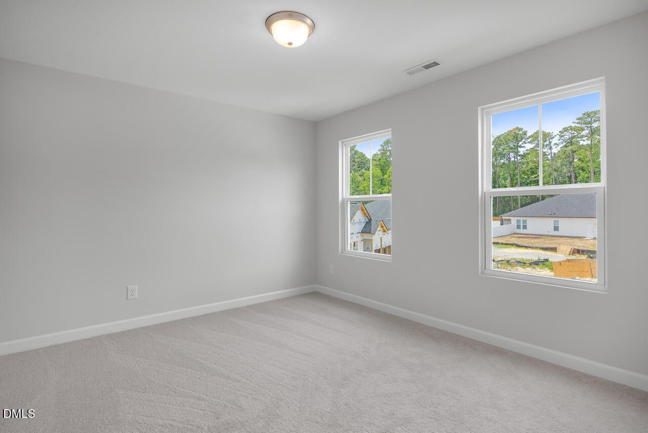 Bright, carpeted bedroom with neutral walls in The Hickory II B home at Wellers Knoll, Lillington, North Carolina.