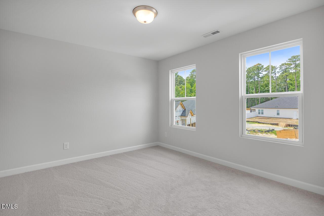 Bright, carpeted bedroom with neutral walls in The Hickory II B home at Wellers Knoll, Lillington, North Carolina.