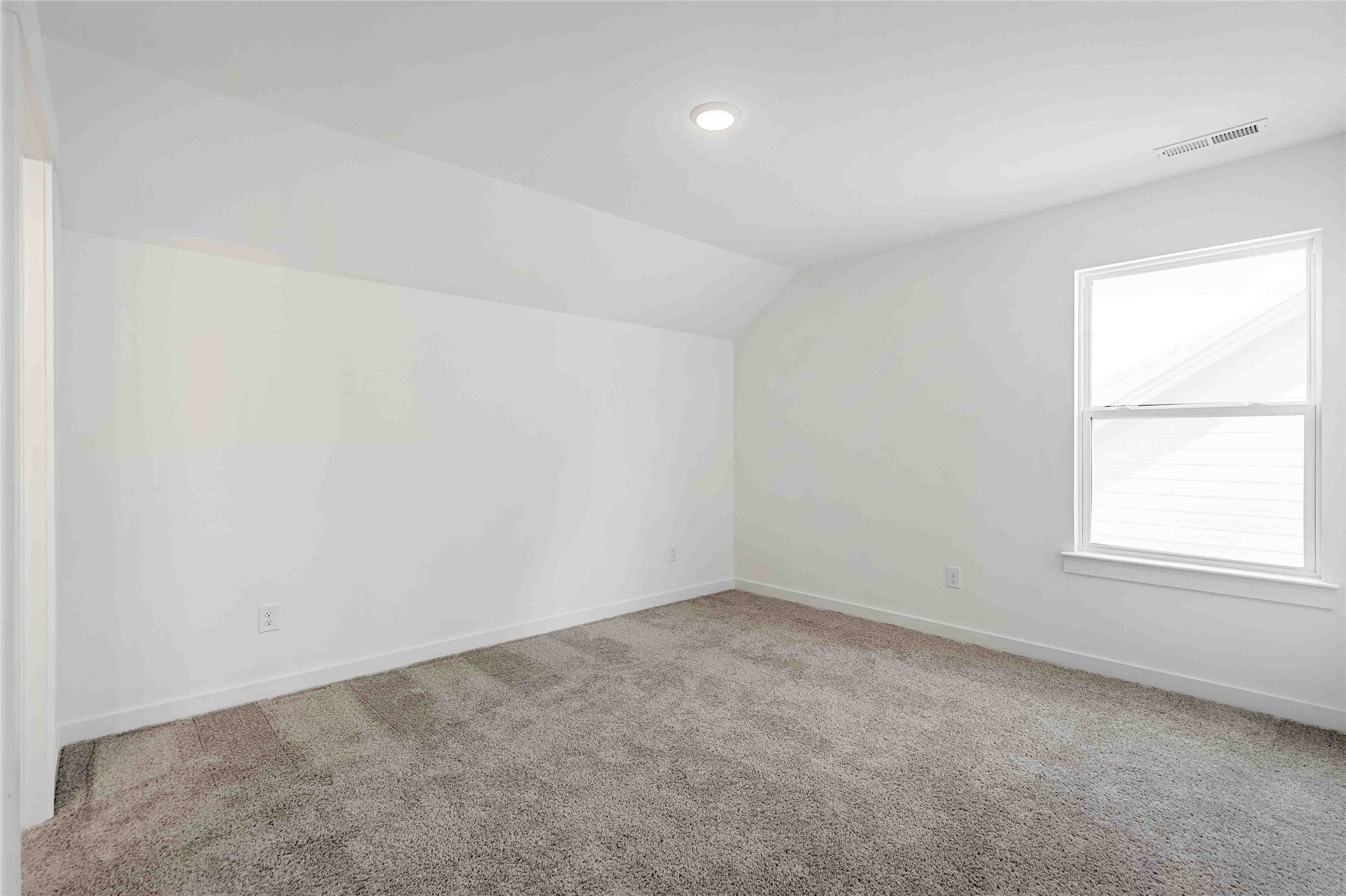 Bright, carpeted bedroom with vaulted ceiling and natural light in The Ash O floor plan at Heartland, Texas.