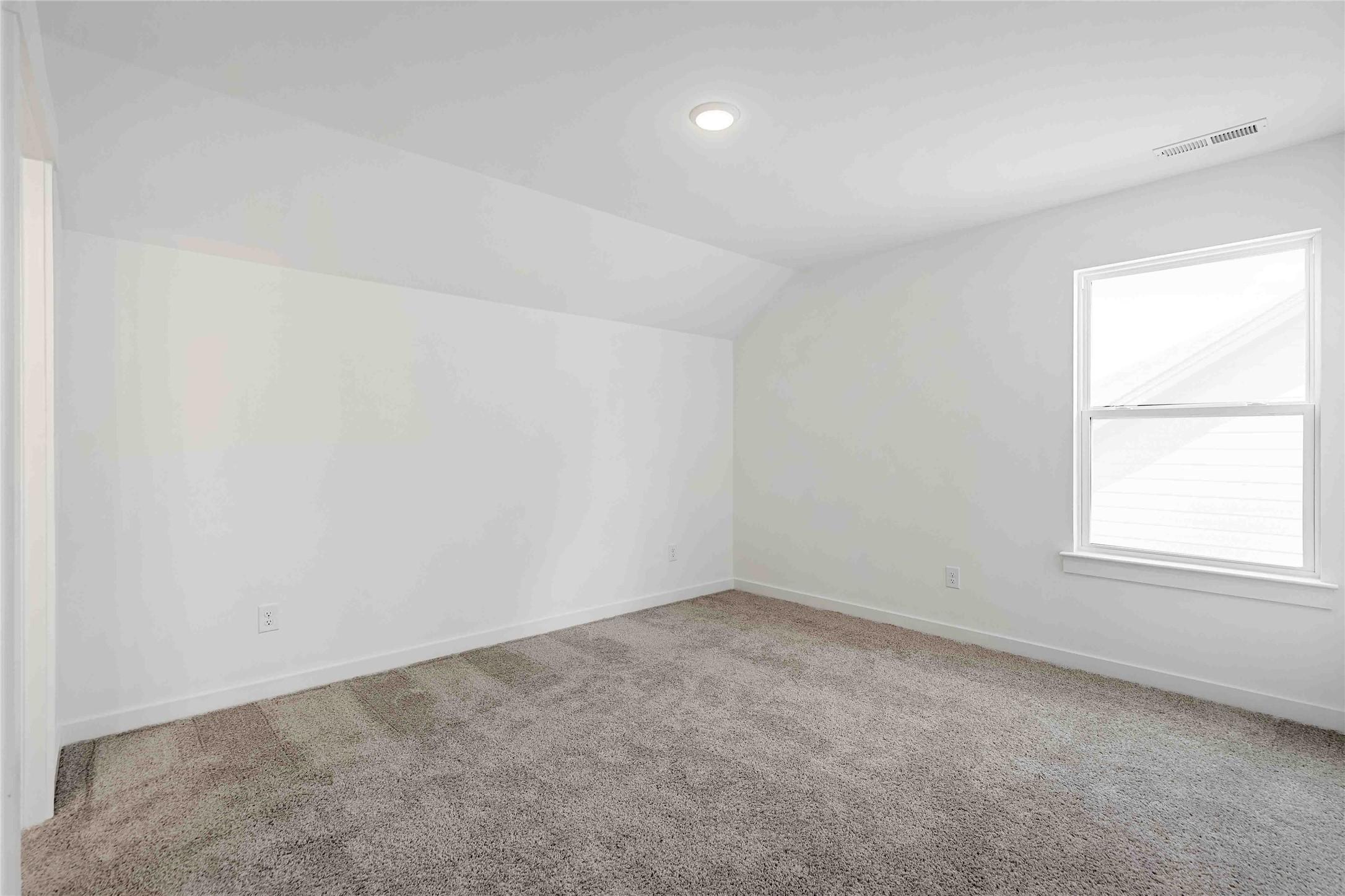 Bright, carpeted bedroom with vaulted ceiling and natural light in The Ash O floor plan at Heartland, Texas.