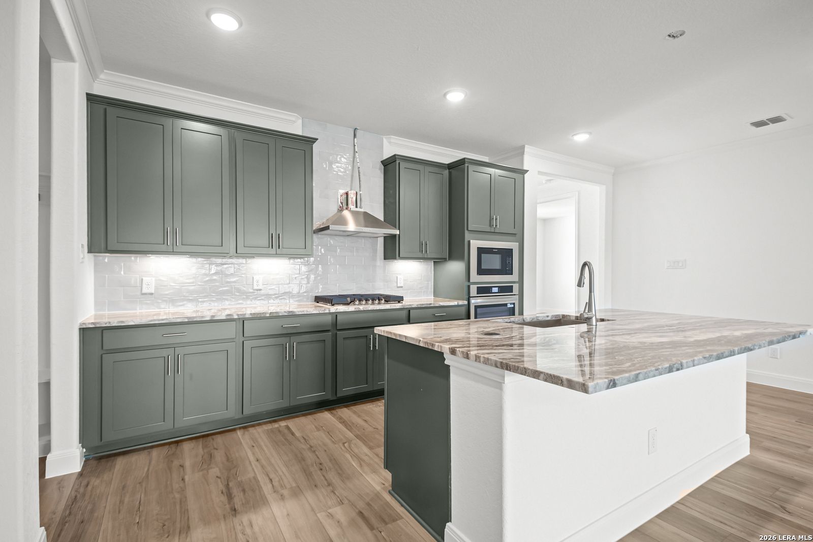 Modern kitchen with sage green cabinets, quartz countertops, and a large island in The Lanier G home, Castroville, Texas.
