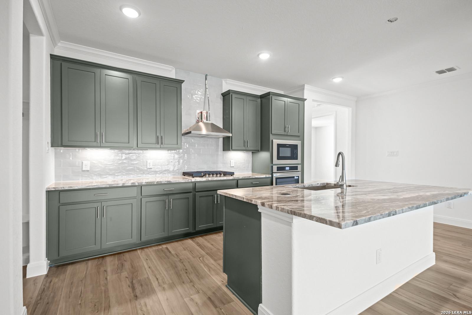 Modern kitchen with sage green cabinets, quartz countertops, and a large island in The Lanier G home, Castroville, Texas.