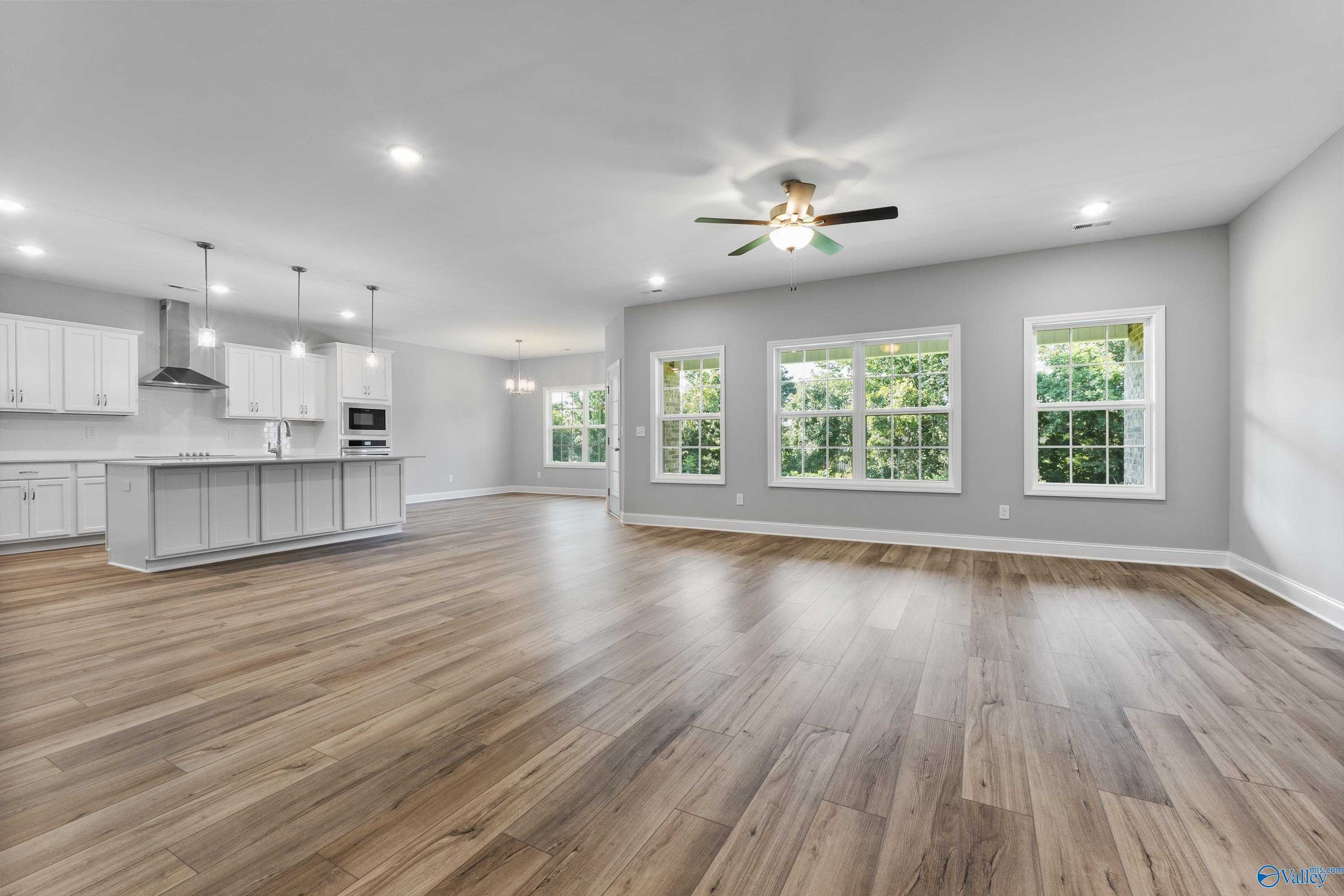 Open-concept living room with kitchen island, white cabinets, hardwood floors, and large windows in Davidson Homes The Rockford, Harvest, AL