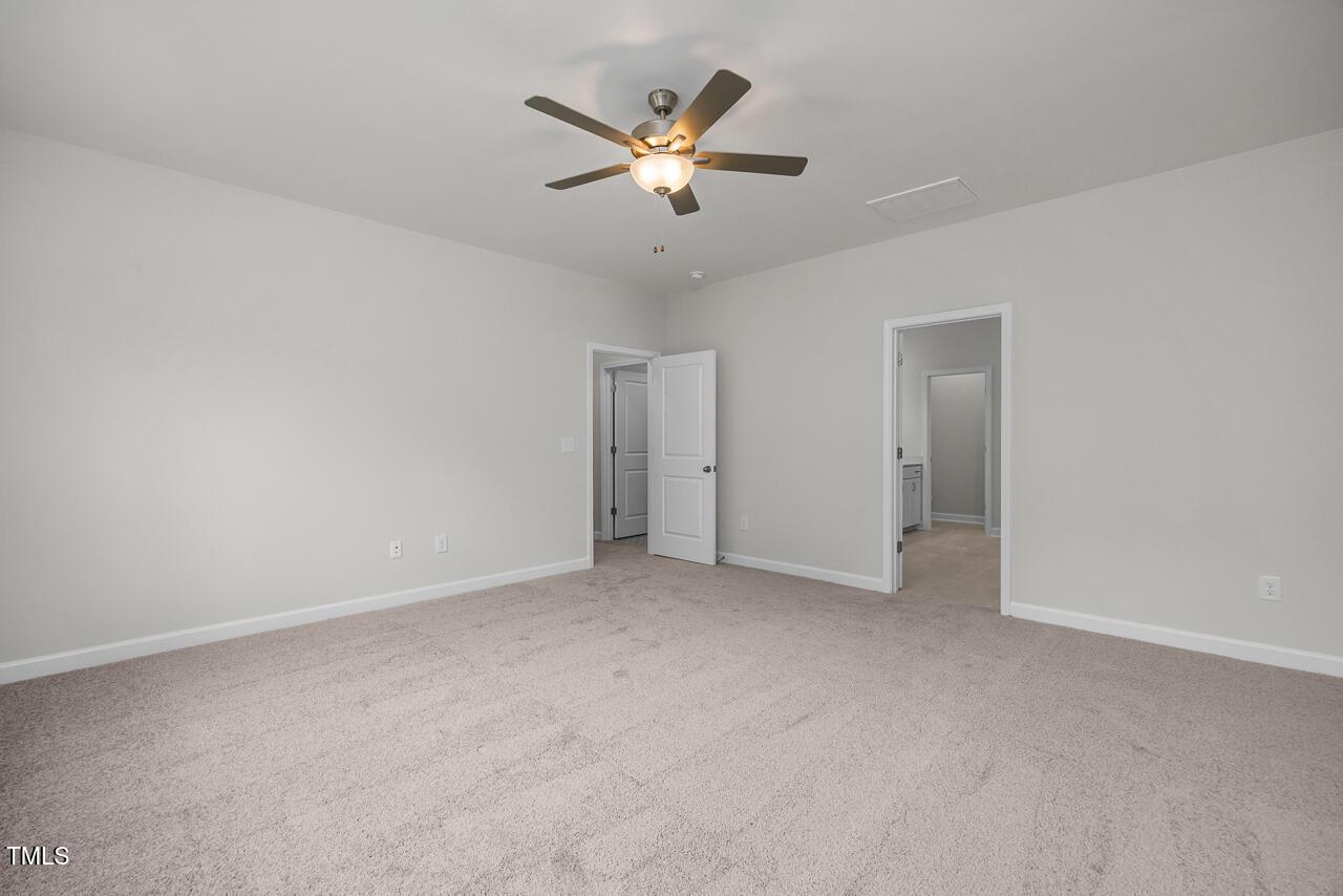 Spacious bedroom with neutral walls, beige carpet, ceiling fan and en-suite door in Davidson Homes The Aspen B, Wake Forest, NC