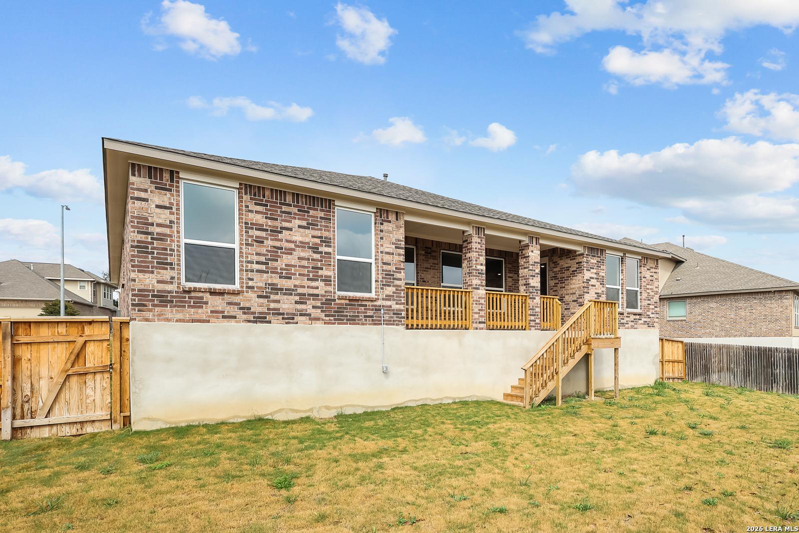Single-story brick home with covered porch, wooden stairs, and fenced yard in Ladera, San Antonio, Texas - Davidson Homes The Rockford G