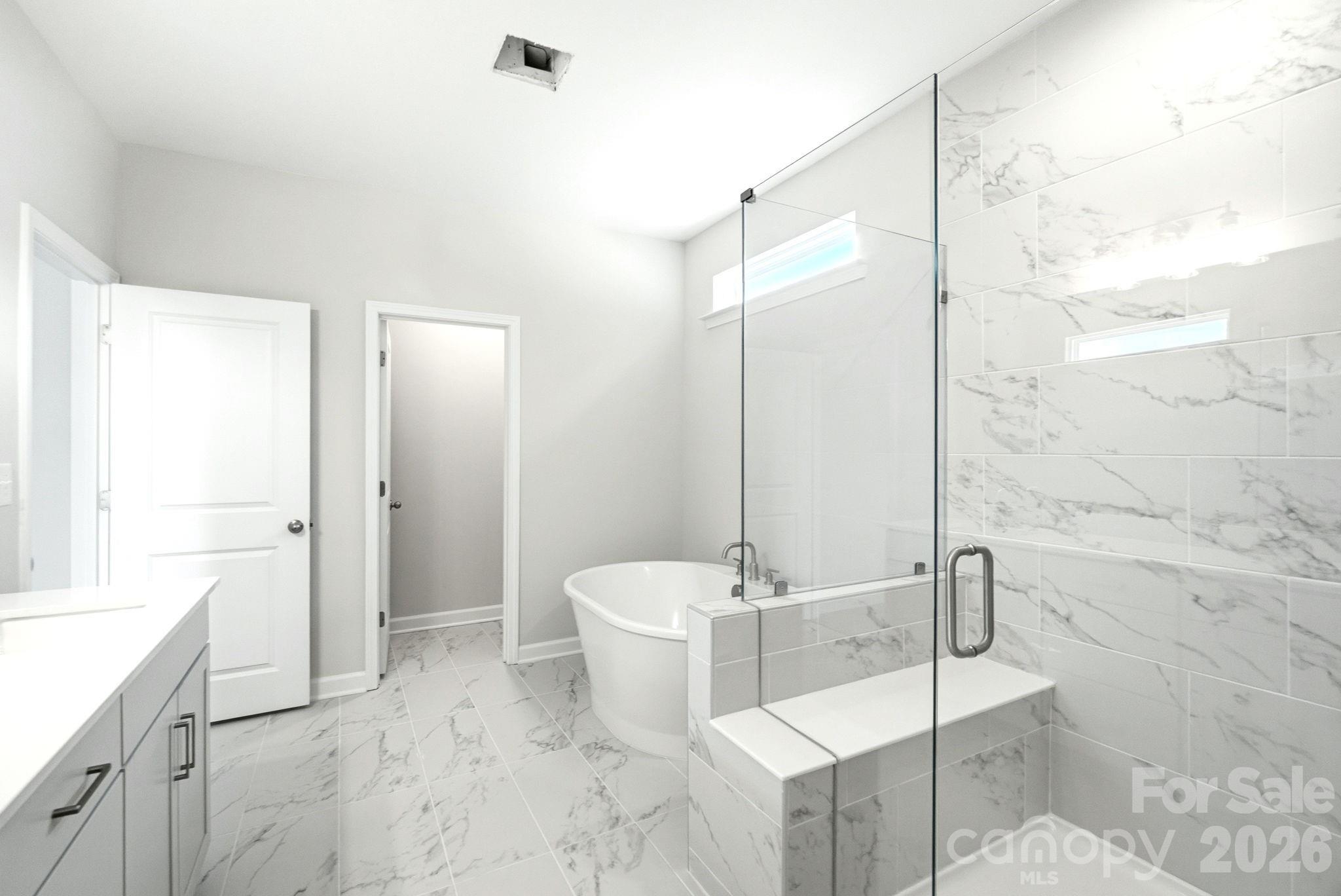 Modern primary bathroom with marble-tiled walk-in shower and soaking tub in The Magnolia B home at Windgate, Mooresville.