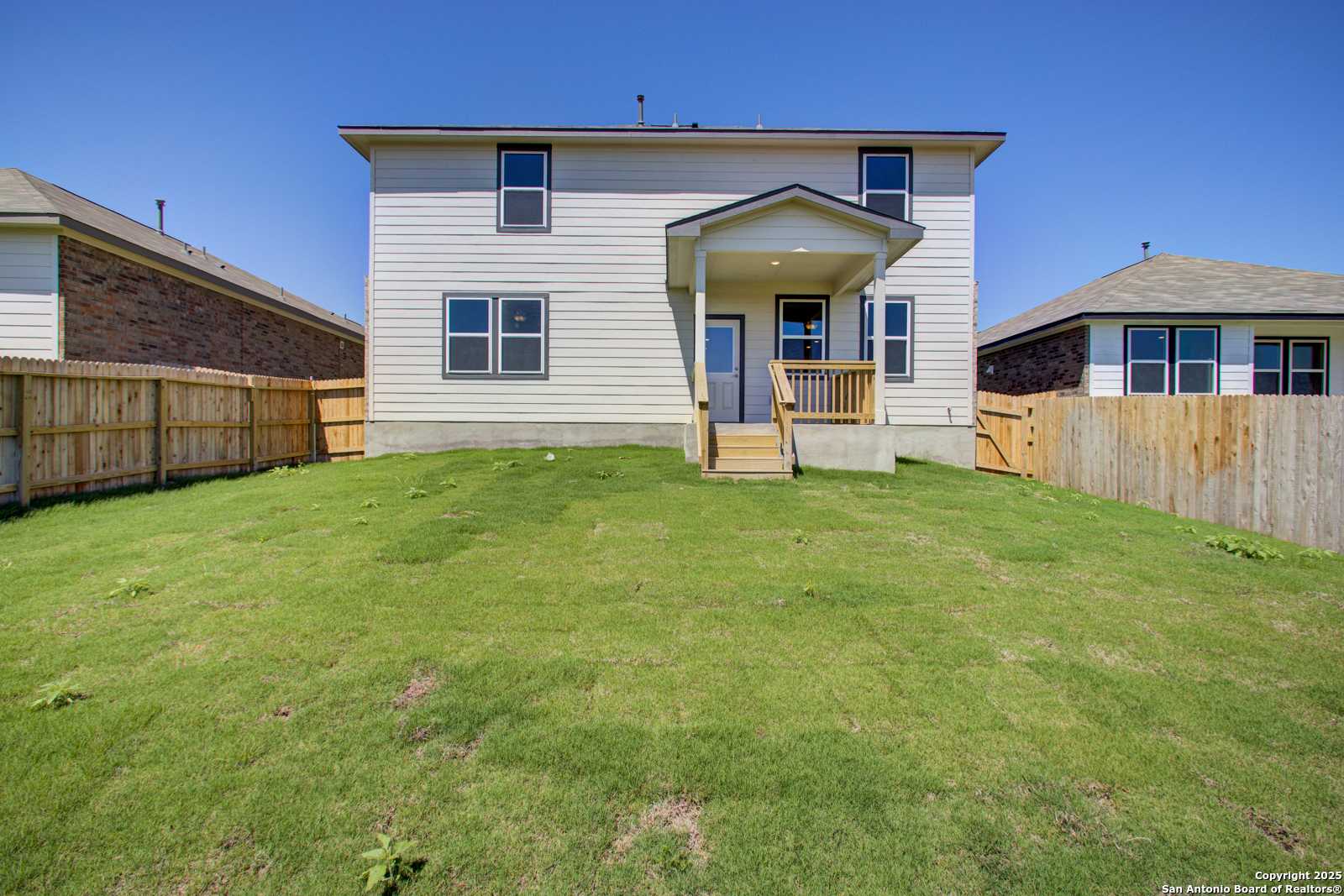 Two-story white home with covered back patio, large green backyard, and wood fences in Comanche Ridge, San Antonio, Texas - Davidson Homes The Douglas G