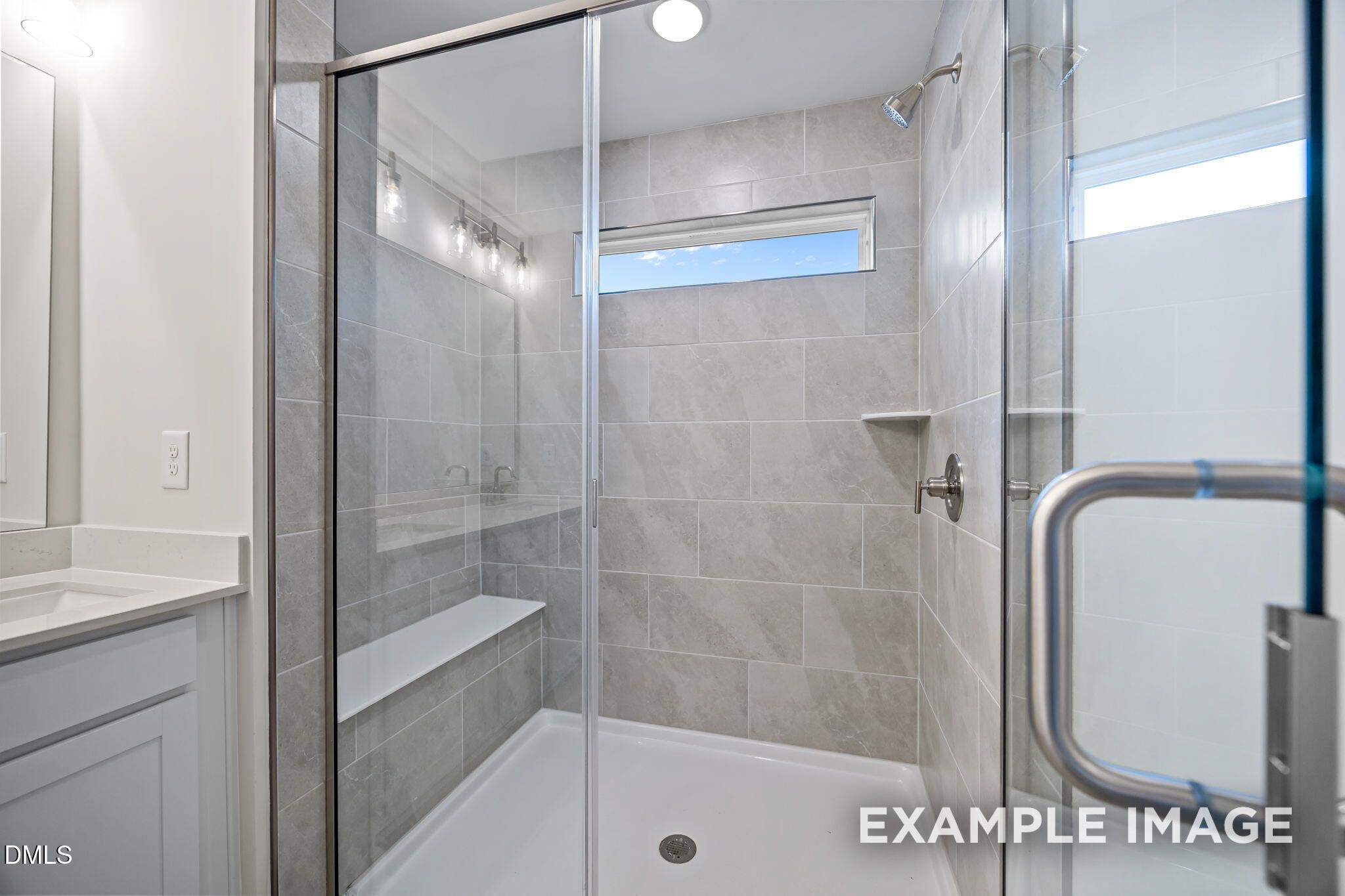 Modern frameless glass shower with gray subway tiles, built-in bench, and rainfall head in Davidson Homes The Avery, Knightdale, NC