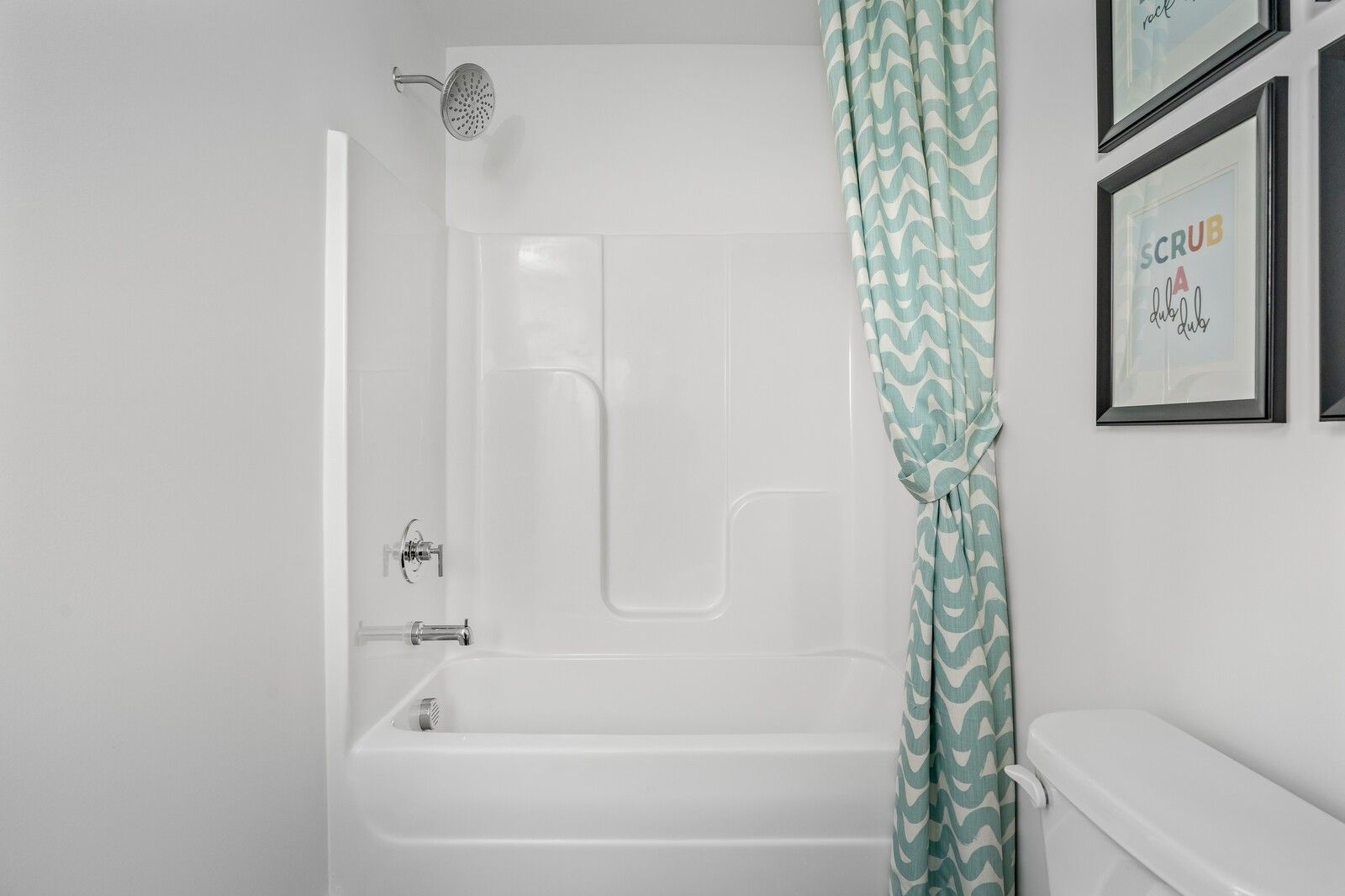 Bright white bathroom with bathtub-shower combo, teal curtain and framed art in Davidson Homes The Cumberland A, Gallatin, TN