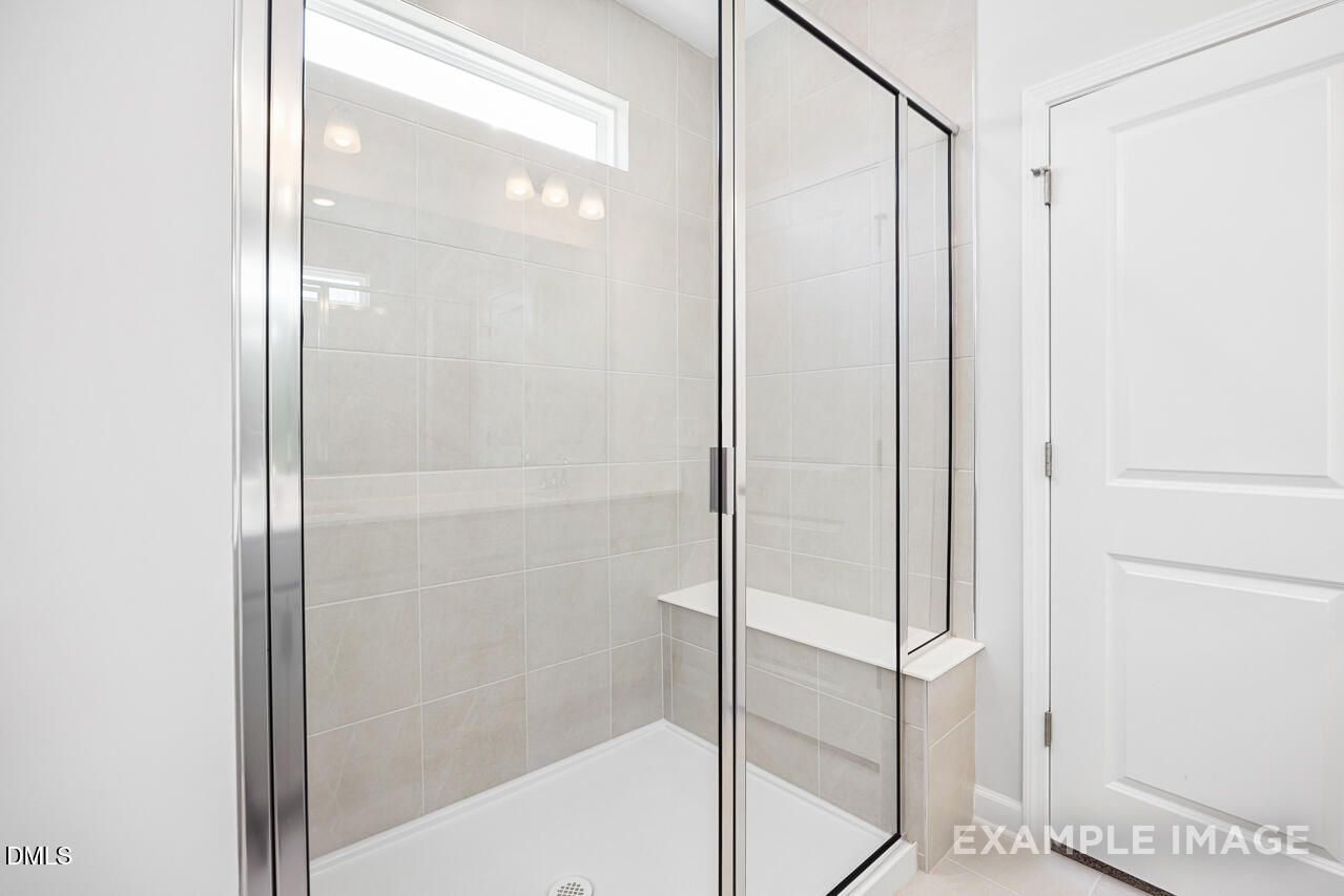 Modern frameless glass walk-in shower with subway tile and bench in master bathroom of The Daphne C, Davidson Homes, Lillington, NC