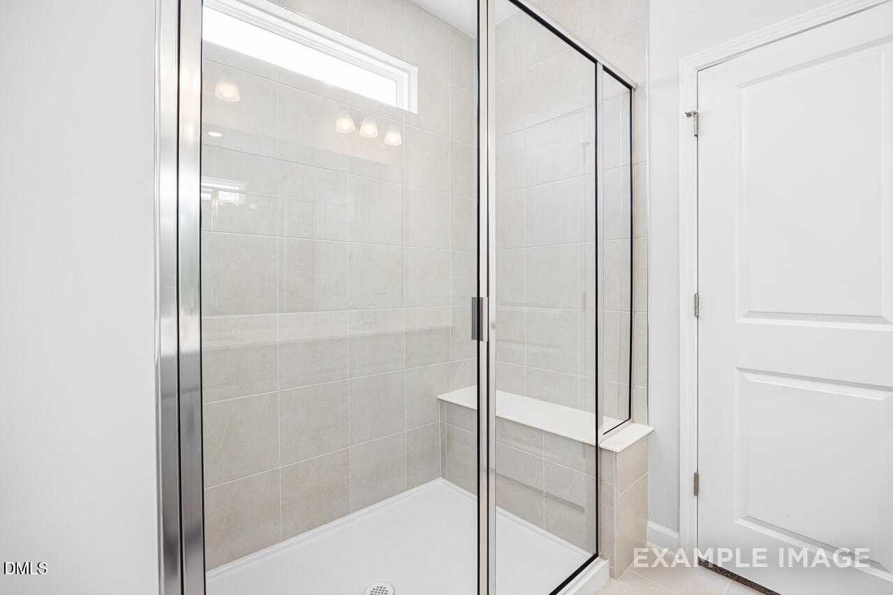Modern frameless glass shower with subway tile walls, built-in bench, and clerestory window in The Daphne C master bath, Lillington, NC