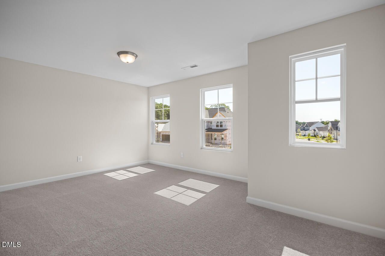 Bright empty bedroom with carpet and large windows overlooking neighborhood homes in Davidson Homes' Willow C, Zebulon NC