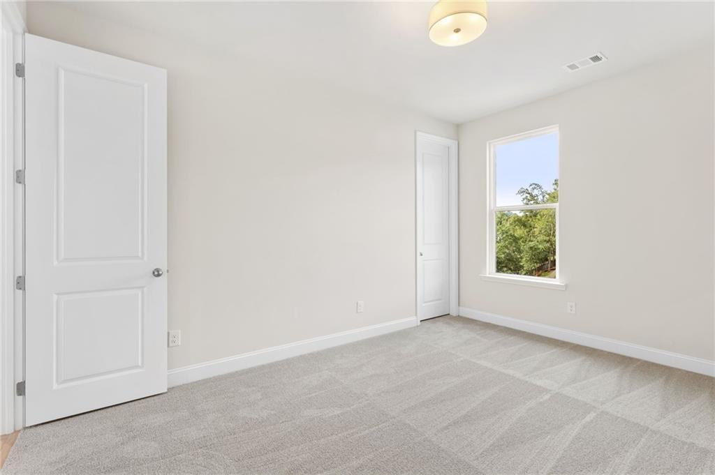 Bright secondary bedroom with large window, neutral walls, and carpeted floor in Davidson Homes The Hampton C, Buford, GA
