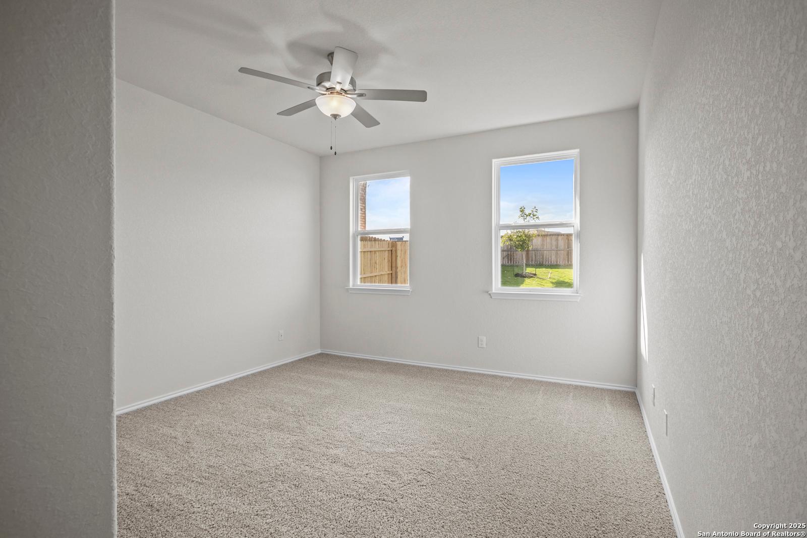 Bright secondary bedroom with ceiling fan, carpeted floor, and windows to fenced backyard in Davidson Homes The Asheville J, San Antonio