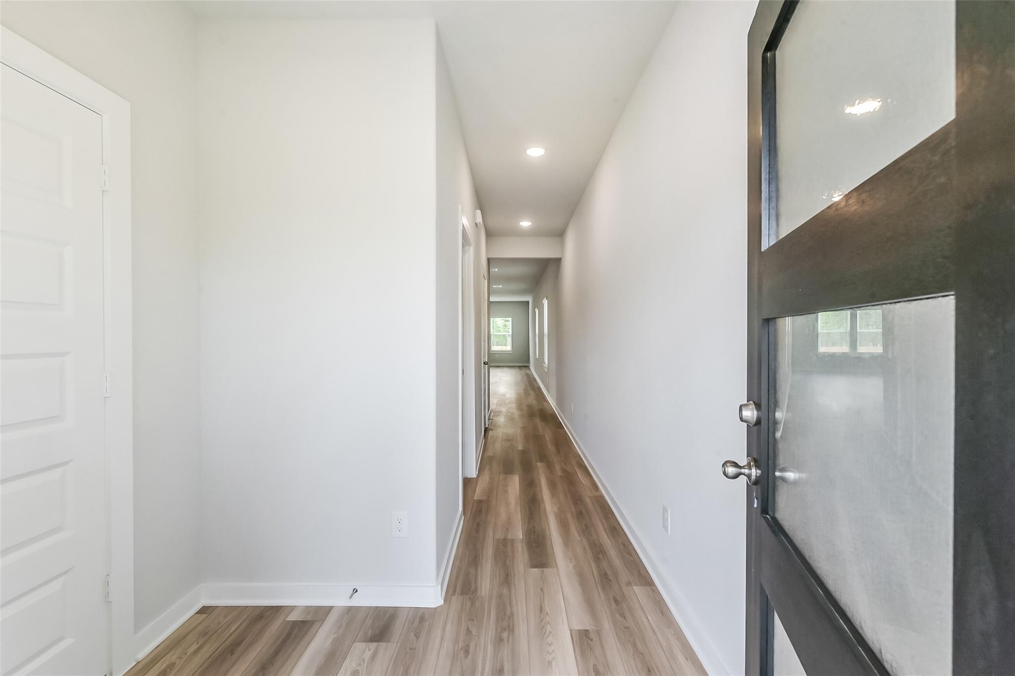 Bright hallway with white walls, hardwood floors, and bedroom doors in Davidson Homes The Frio G, Windmill Estates, Magnolia TX