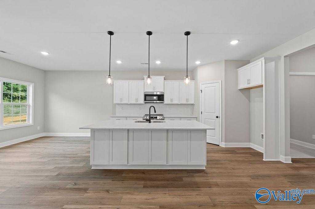 Modern white shaker kitchen with oversized island sink, pendant lights, and hardwood floors in Davidson Homes Montgomery B, Hartselle, AL