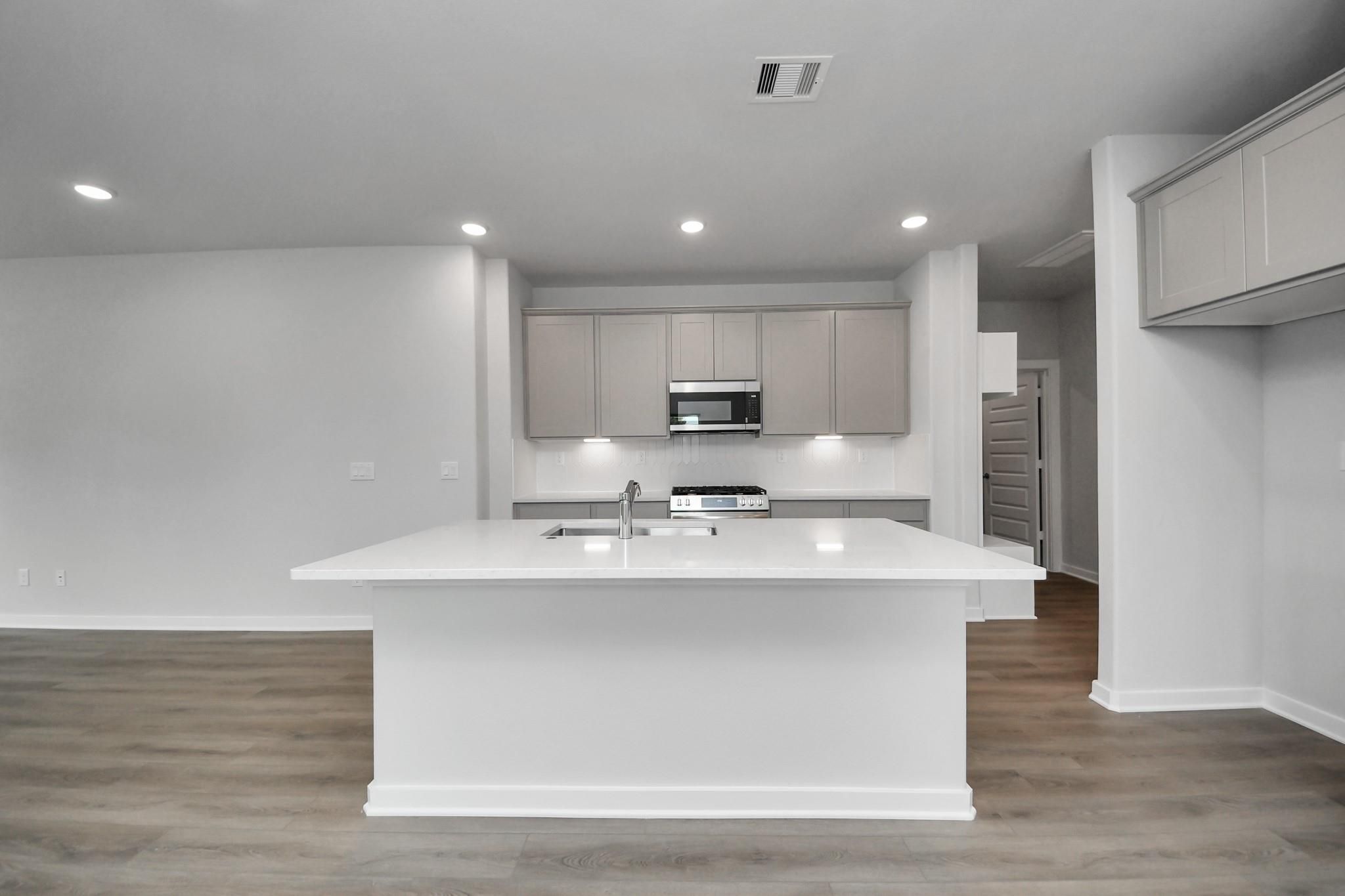 Bright open-concept kitchen with white island, gray shaker cabinets, and stainless appliances in Davidson Homes The Blanco E, Magnolia, TX