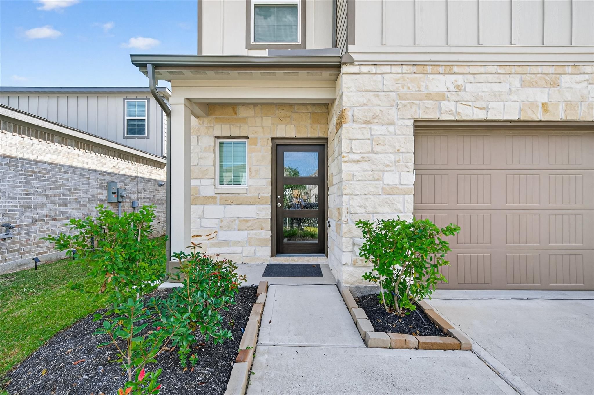 Modern two-story front exterior of The Brazos E home featuring stone accents, 2-car garage, and landscaped walkway in Lakes at Black Oak, Magnolia, Texas