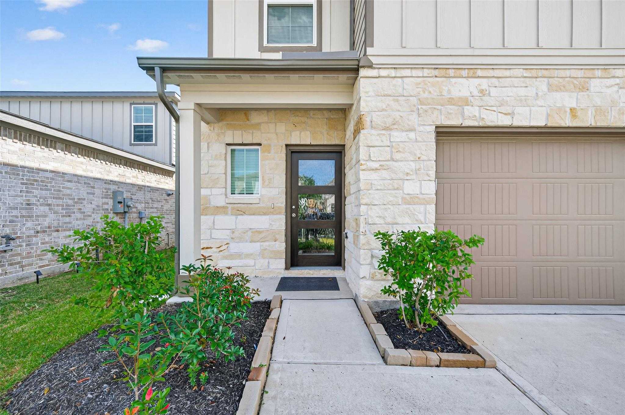 Modern two-story front exterior of The Brazos E home featuring stone accents, 2-car garage, and landscaped walkway in Lakes at Black Oak, Magnolia, Texas