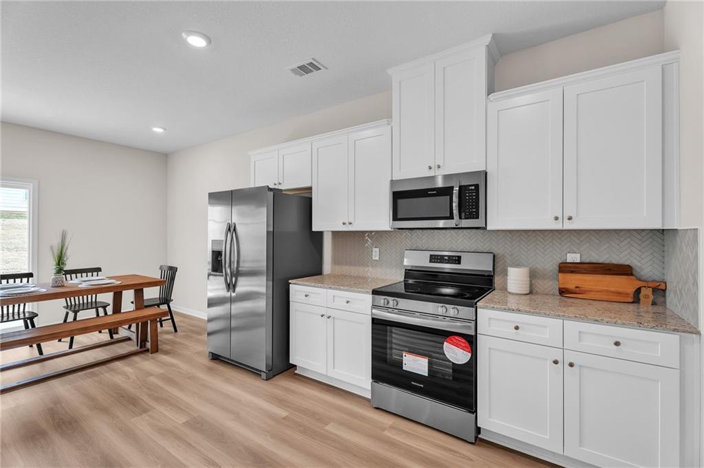 Modern kitchen with white shaker cabinets, stainless steel appliances, quartz counters, and adjacent dining area in The Bartlett home, Phenix City
