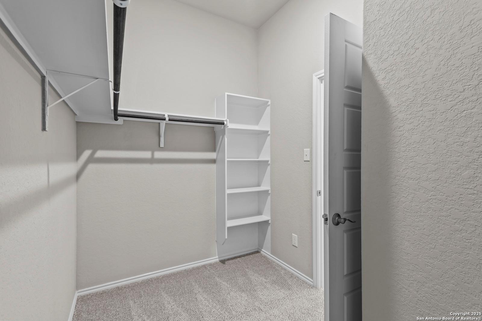 Spacious walk-in closet with built-in white shelves and hanging rods in The Collin B home, Hannah Heights, Seguin, Texas