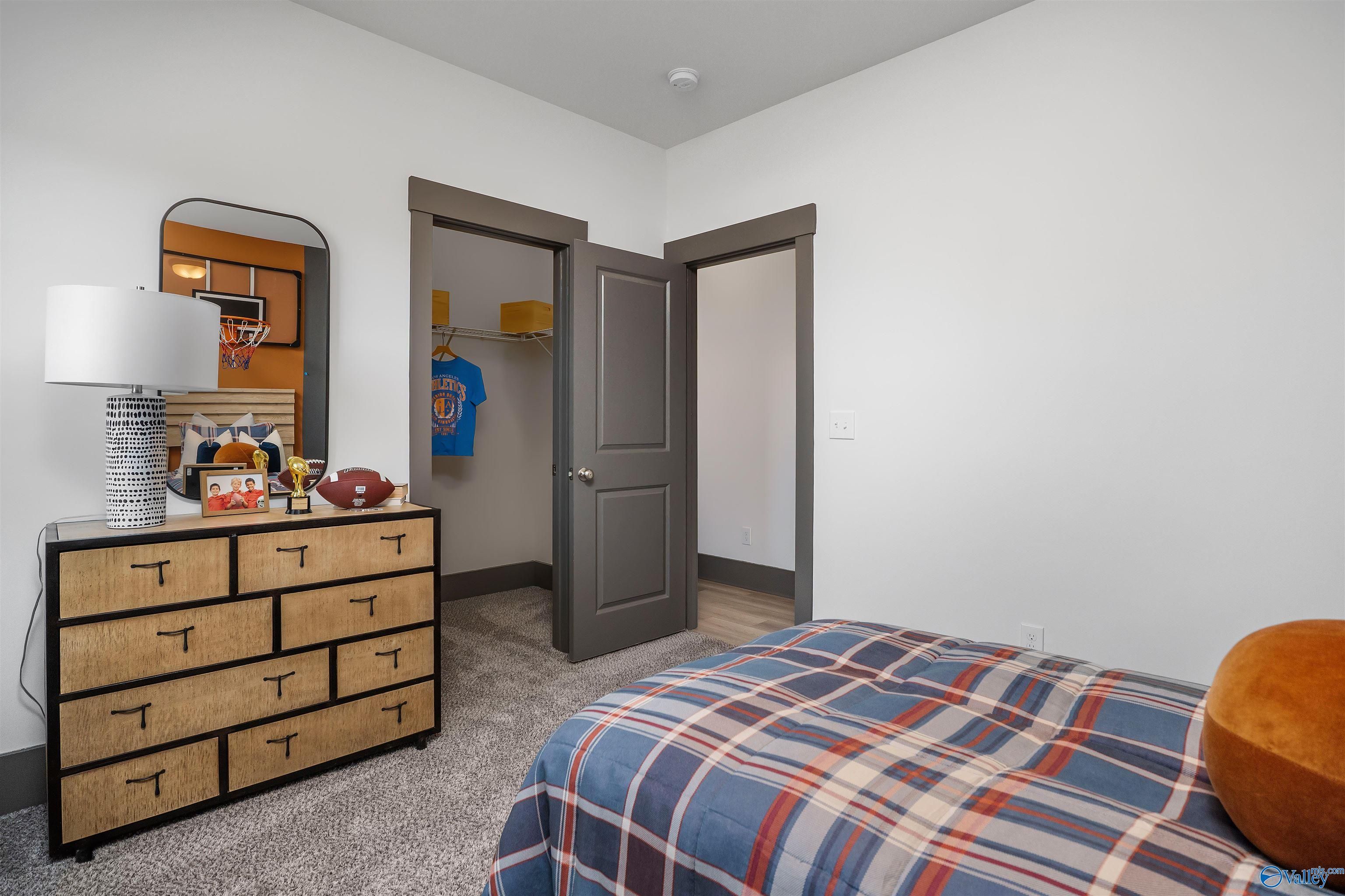 Cozy sports-themed bedroom with wooden dresser, plaid bed, basketball jersey, and closet in Davidson Homes The Rockford B, Madison, AL