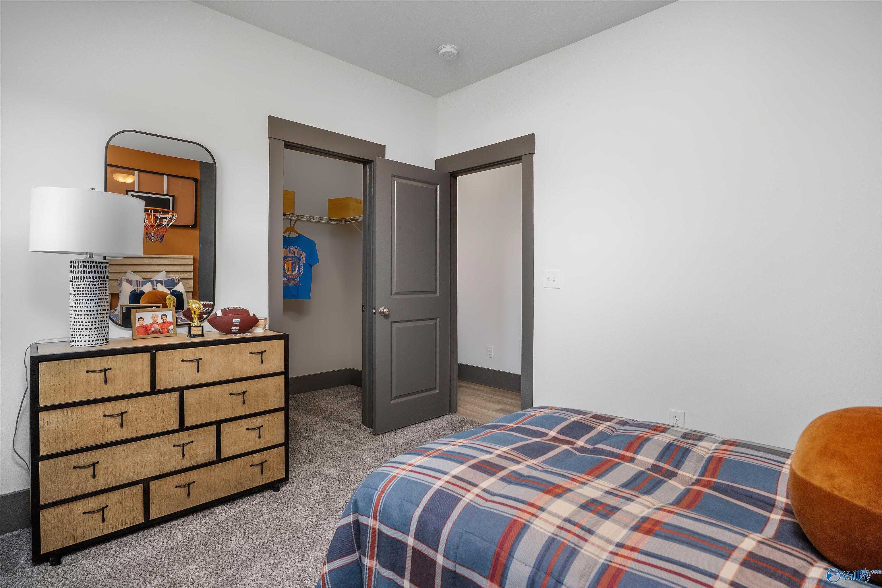 Cozy sports-themed bedroom with wooden dresser, plaid bed, basketball jersey, and closet in Davidson Homes The Rockford B, Madison, AL