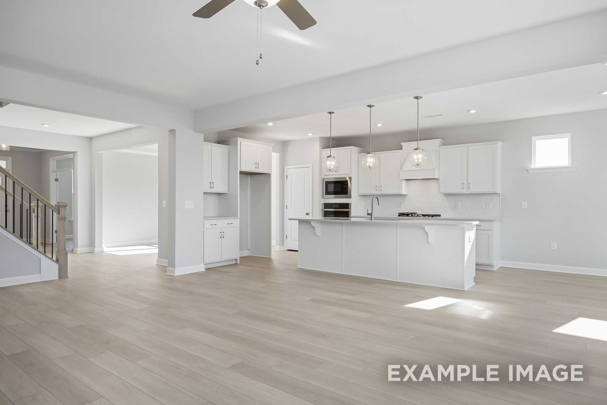 Open-concept kitchen in The Cypress D II with white cabinets, large island, stainless steel appliances, and hardwood floors