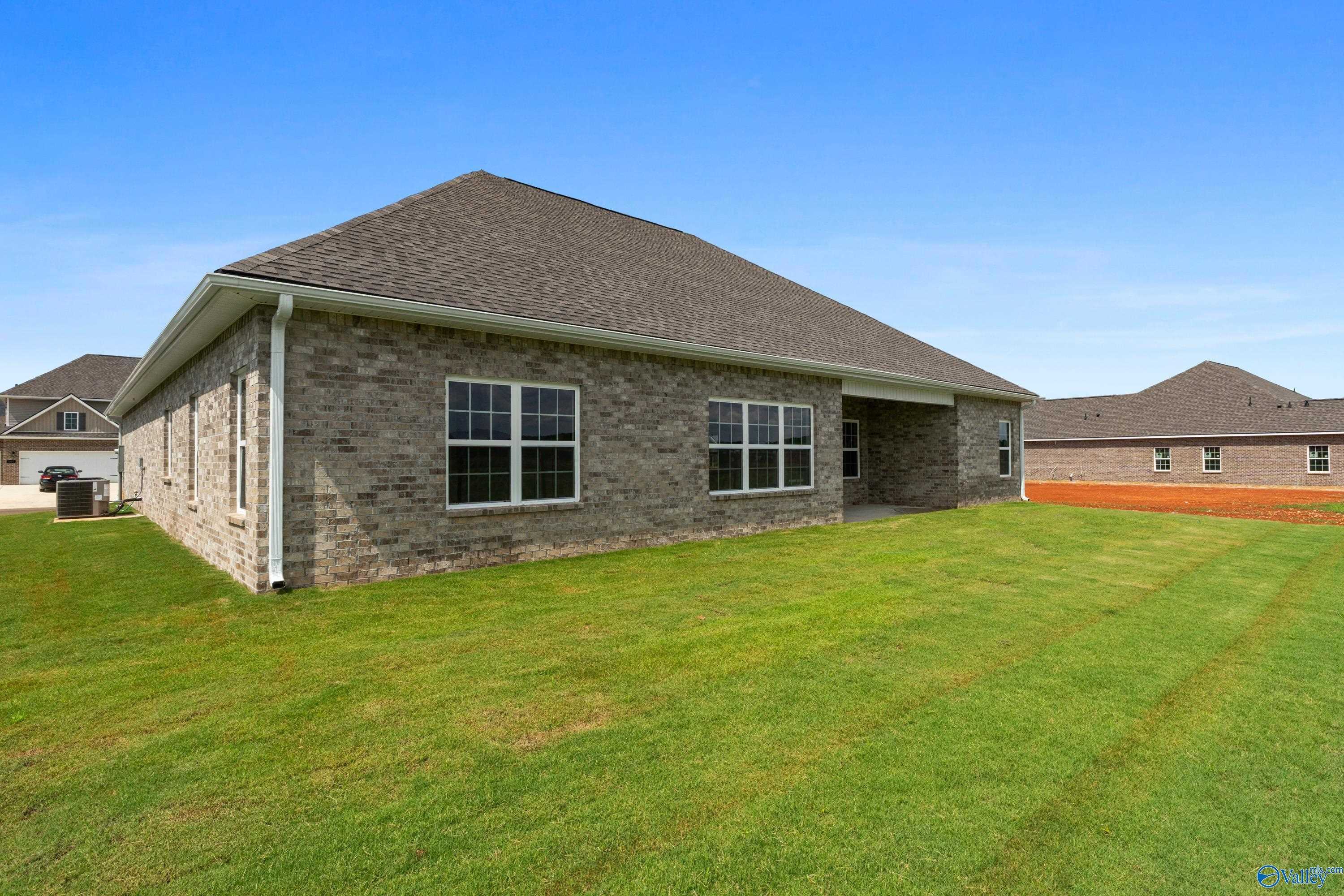 Side view of single-story brick The Finleigh home by Davidson Homes, covered patio, lush green lawn in Kendall Farms, Toney, Alabama