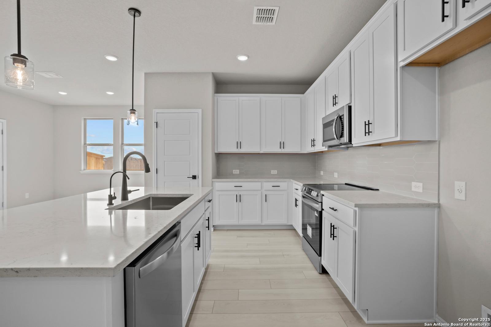 Modern white kitchen with quartz island, stainless steel appliances, pendant lights in The Daphne H, Seguin, Texas
