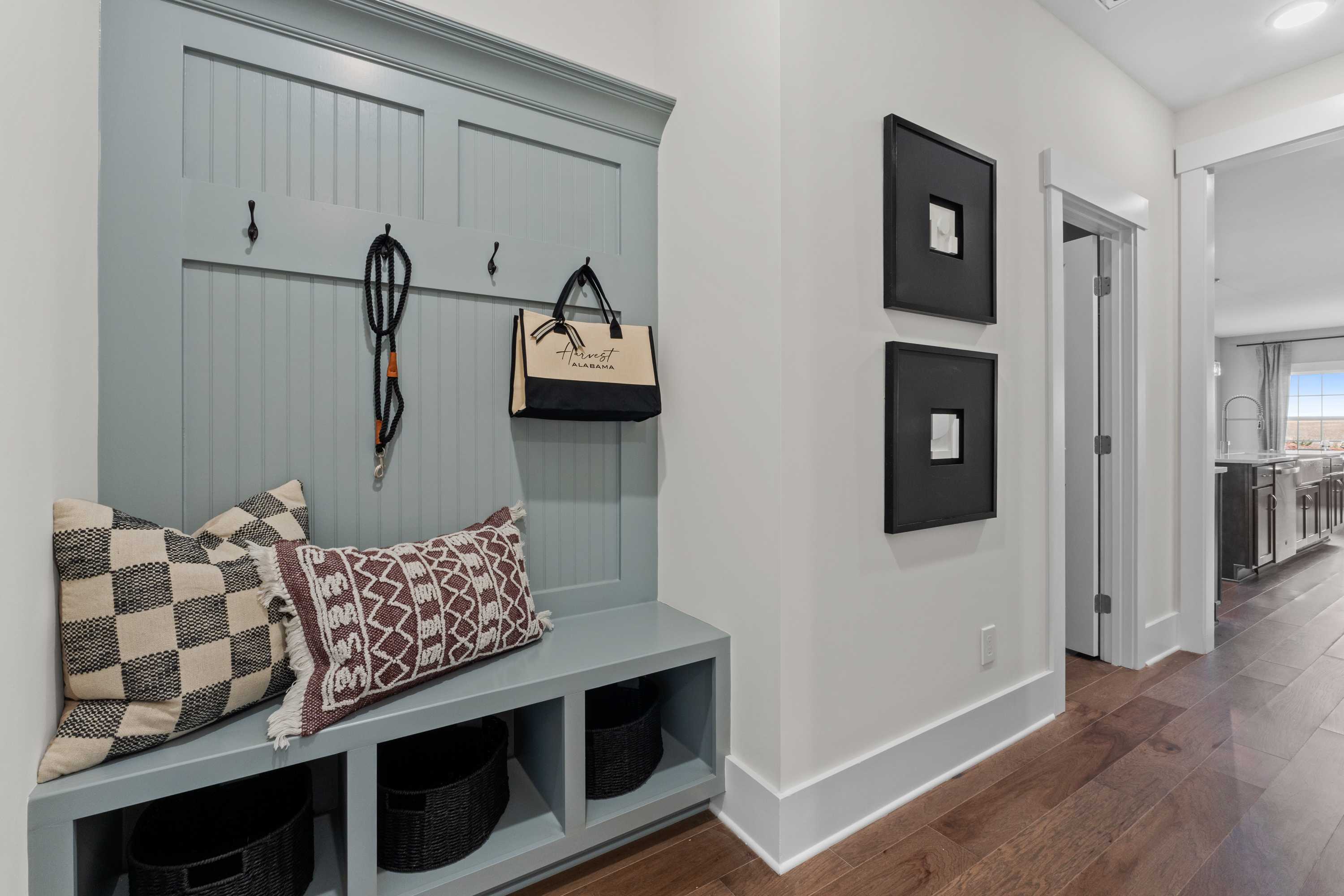Cozy blue shiplap mudroom bench with hooks, patterned pillows, and storage baskets in Creekside Harvest AL home