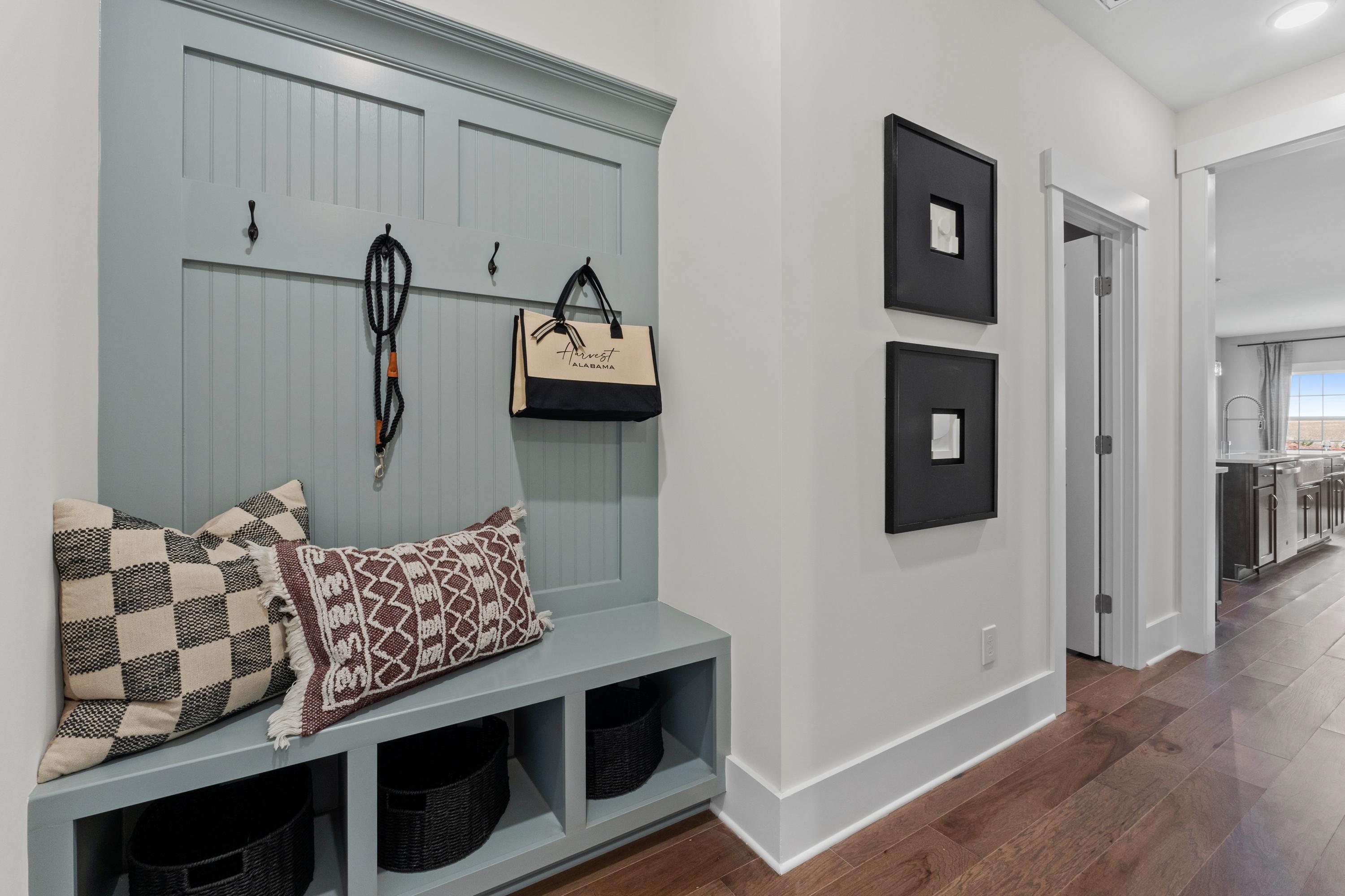 Cozy blue shiplap mudroom bench with hooks, patterned pillows, and storage baskets in Creekside Harvest AL home