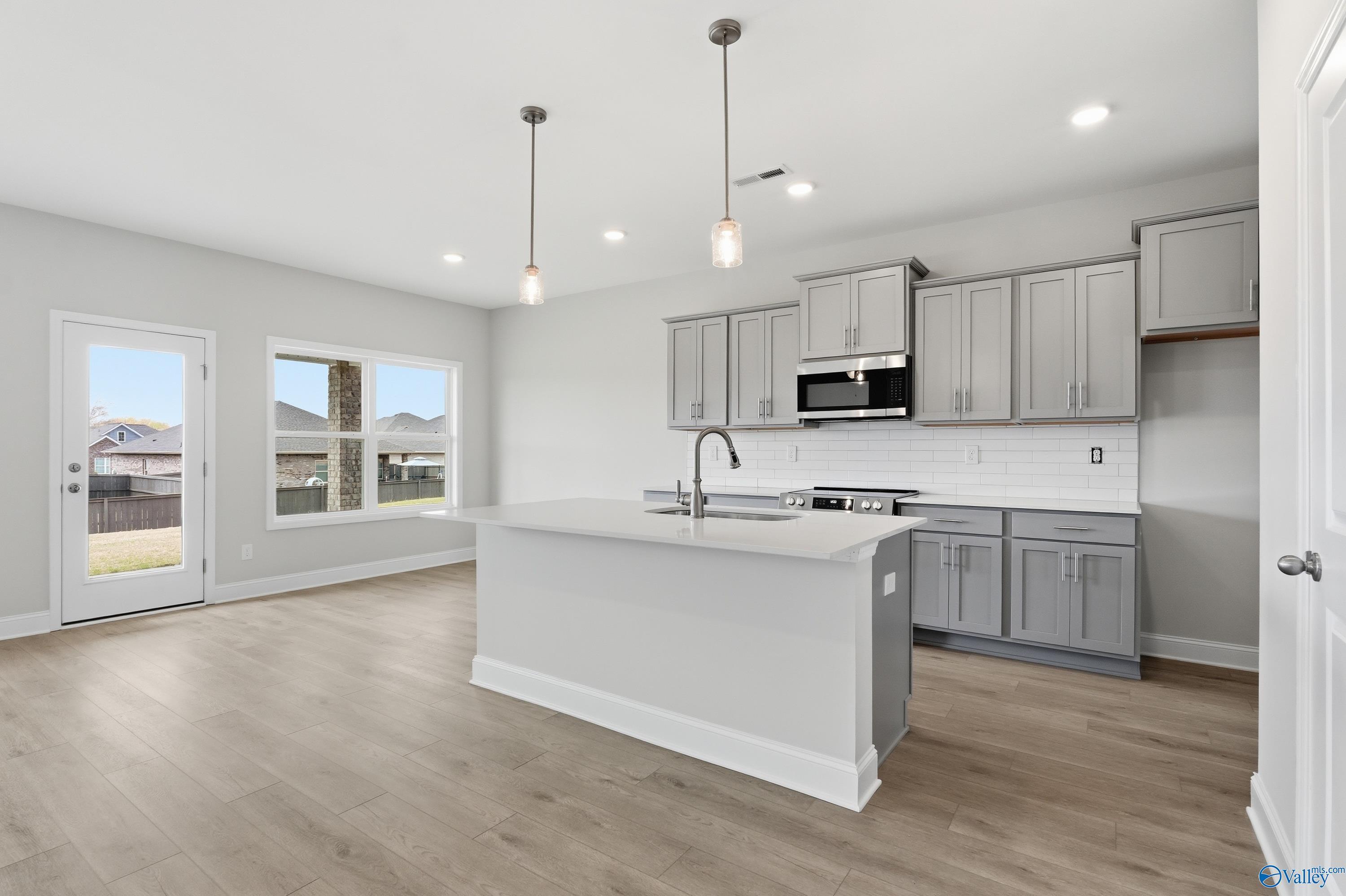 Modern open-concept kitchen with gray cabinets, white island sink, stainless appliances, and large windows in Davidson Homes Shelby B, New Market, AL