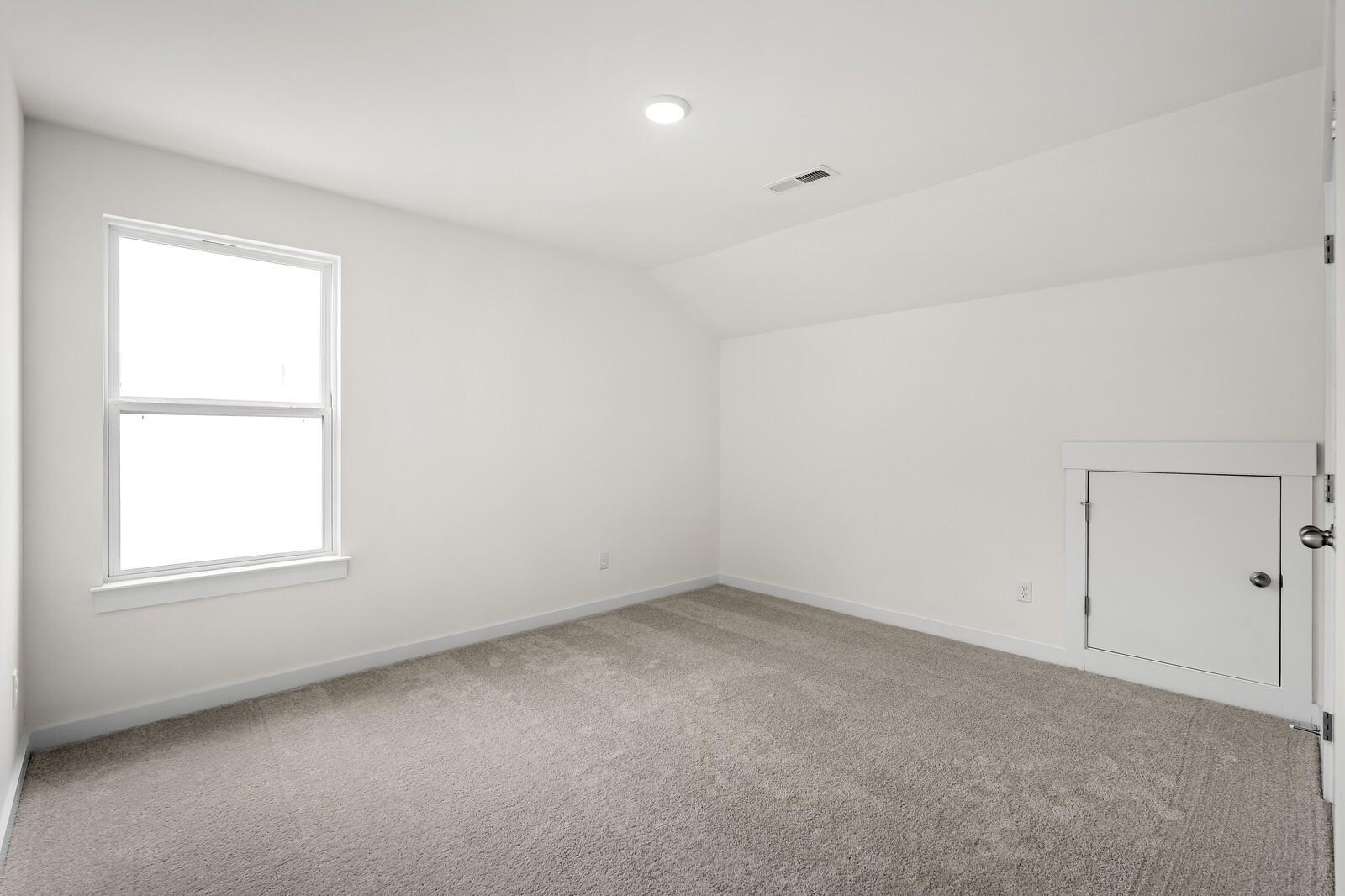 Bright secondary bedroom with sloped ceiling, large window, beige carpet, built-in closet in Davidson Homes The Ridgeport, Gallatin, TN