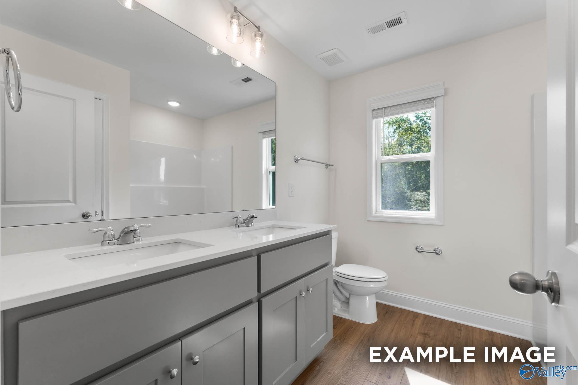 Bright modern bathroom with double quartz vanity, gray cabinets, large mirror, and window in Davidson Homes The Shelby A, Hazel Green, Alabama