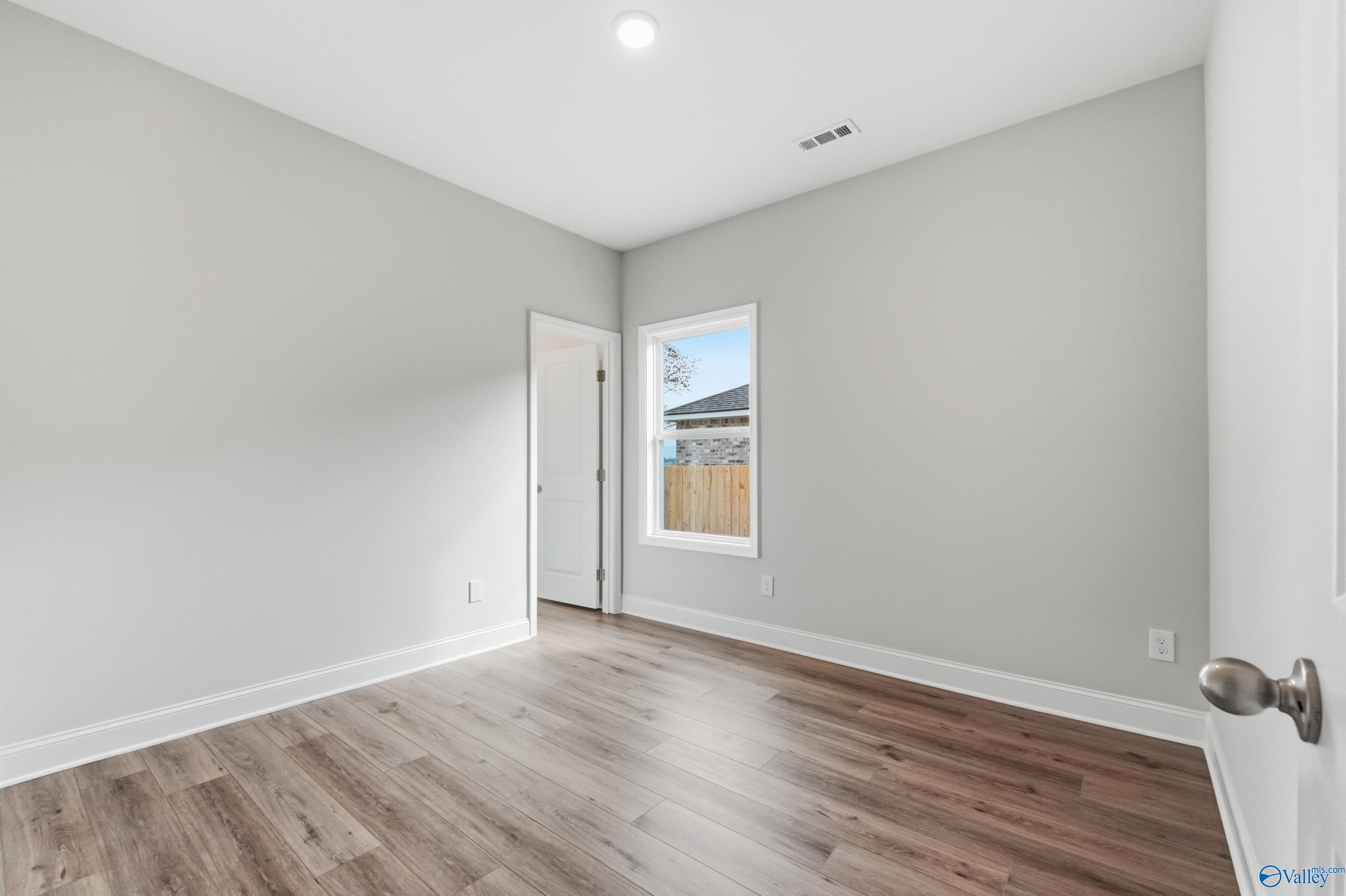 Bright secondary bedroom featuring light gray walls, hardwood floors, and window with backyard view in Davidson Homes The Daphne C, Toney, Alabama