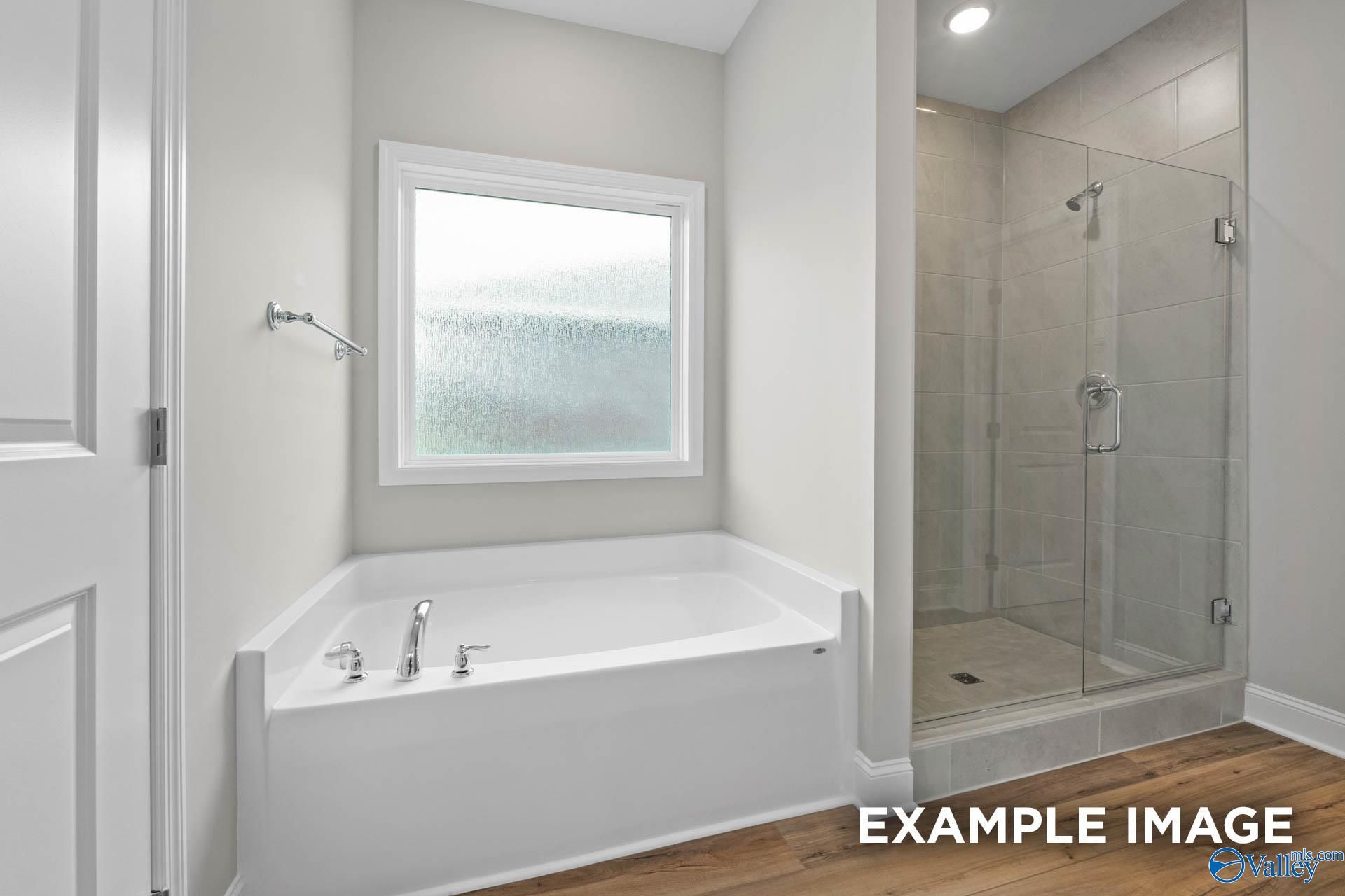 Elegant master bathroom featuring corner soaking tub, glass-enclosed walk-in shower, and frosted window in Davidson Homes The Everett, Meridianville, Alabama
