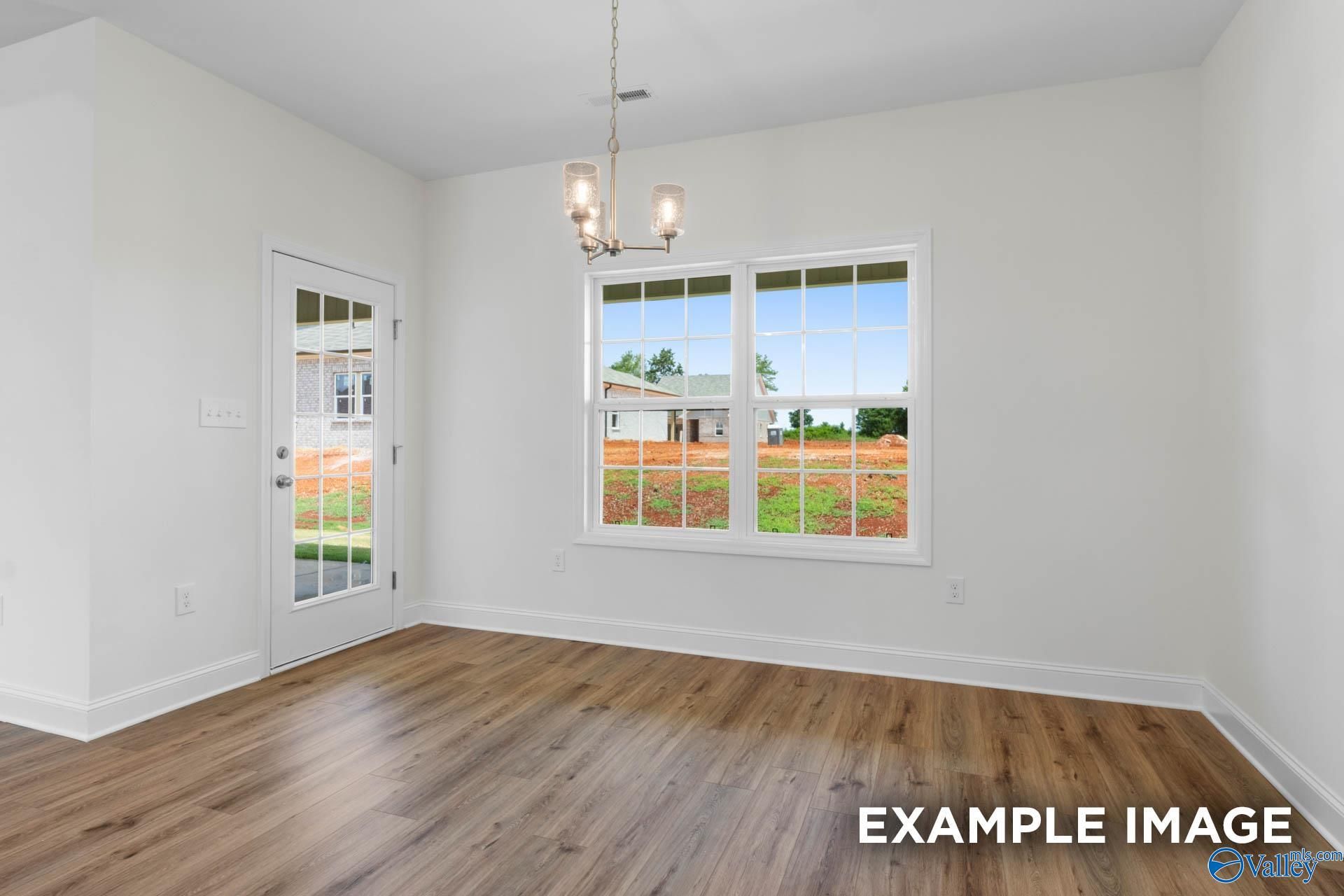 Bright sunroom with white walls, hardwood floors, modern chandelier, and large window view of green backyard in Davidson Homes The Oxford, Huntsville