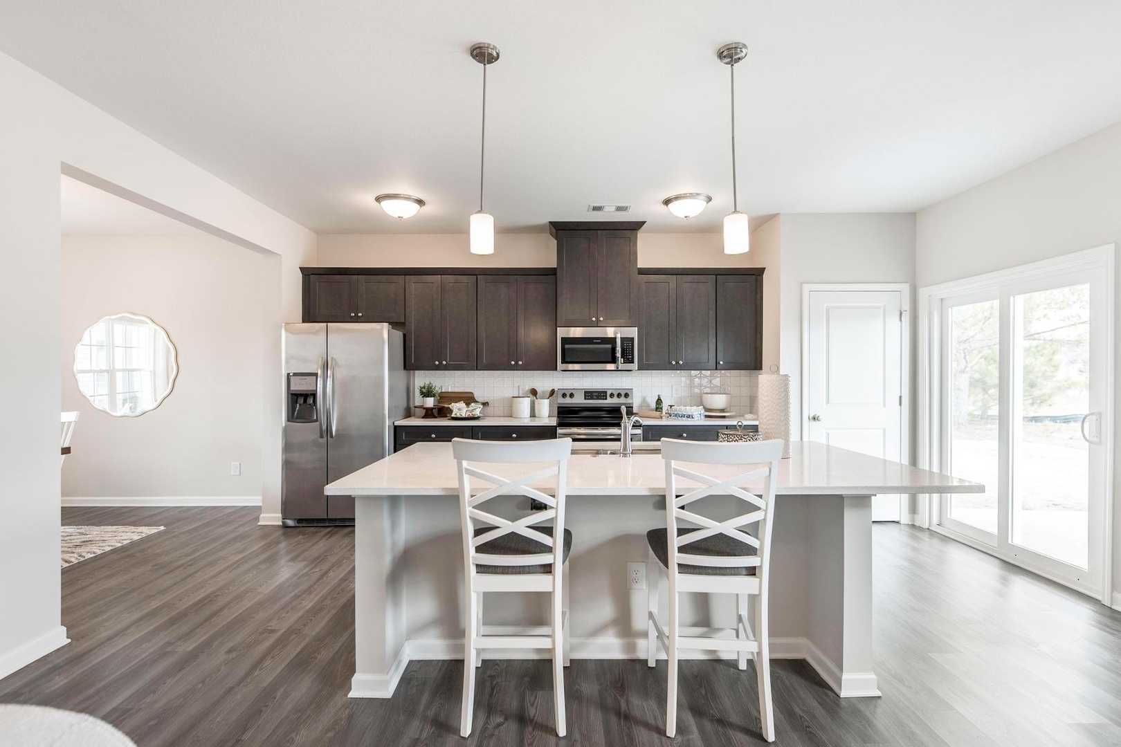 Spacious modern kitchen at Cape Reserve Donahue Ridge in Auburn AL with dark cabinets white quartz island hardwood floors and stainless appliances