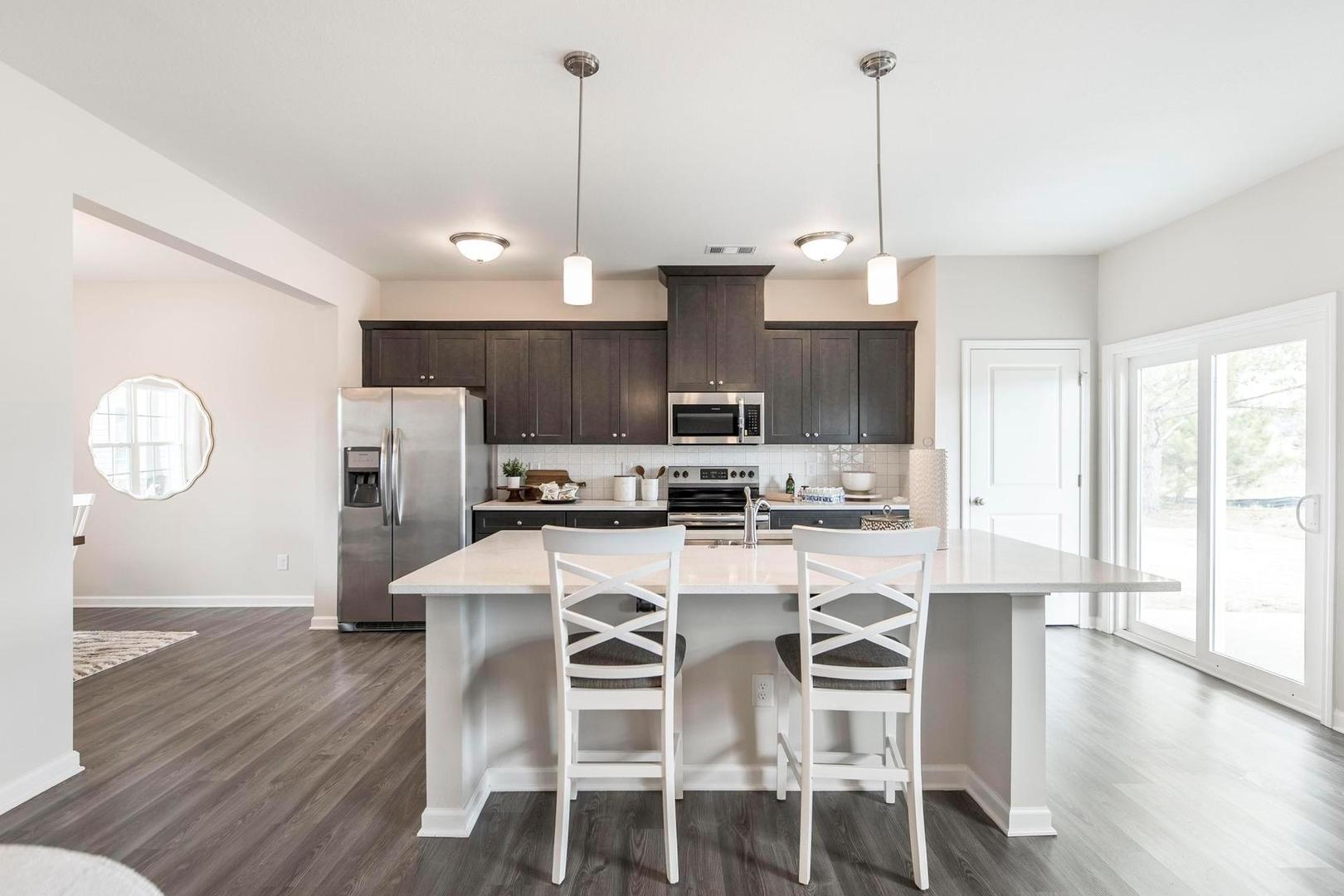 Spacious modern kitchen at Cape Reserve Donahue Ridge in Auburn AL with dark cabinets white quartz island hardwood floors and stainless appliances