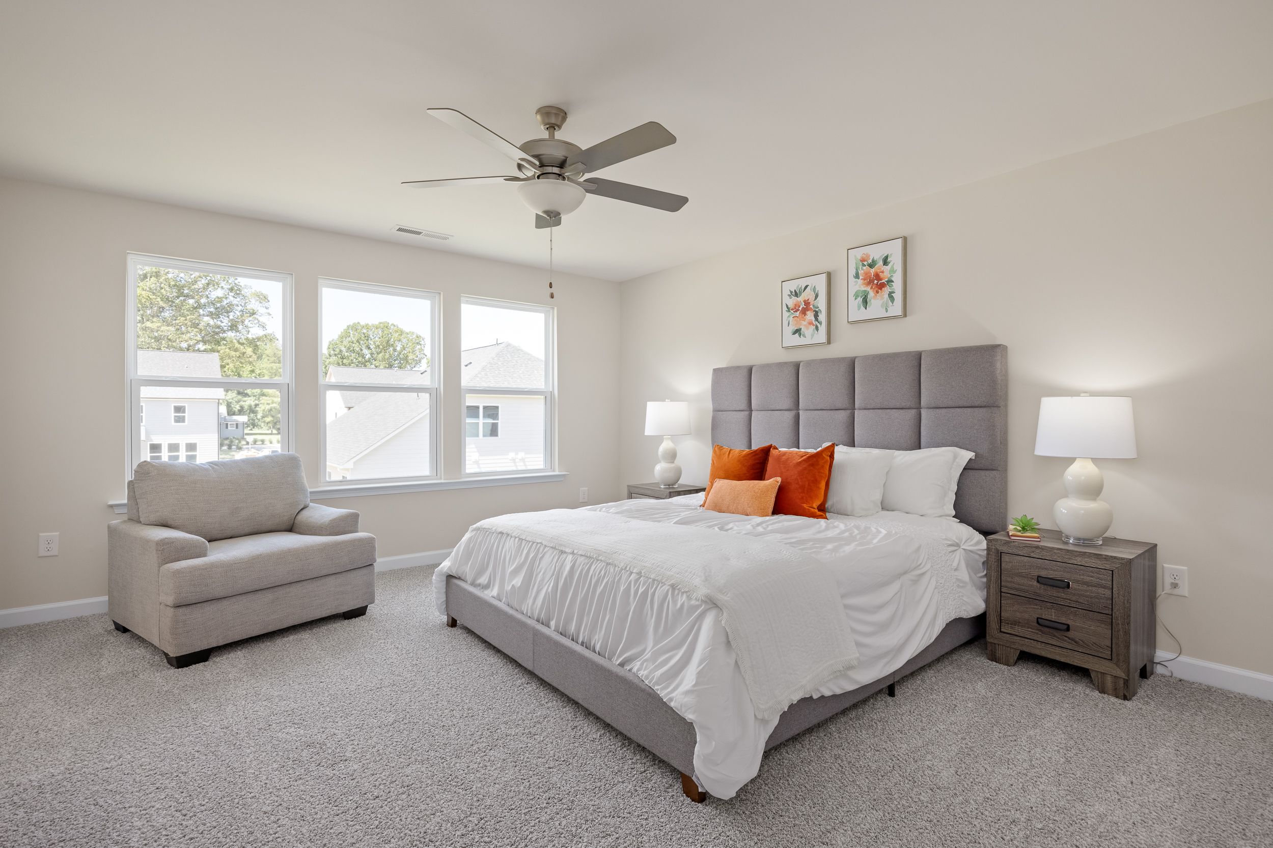 Spacious primary bedroom in Montrose Aberdeen NC with gray tufted headboard orange accent pillows ceiling fan and large windows
