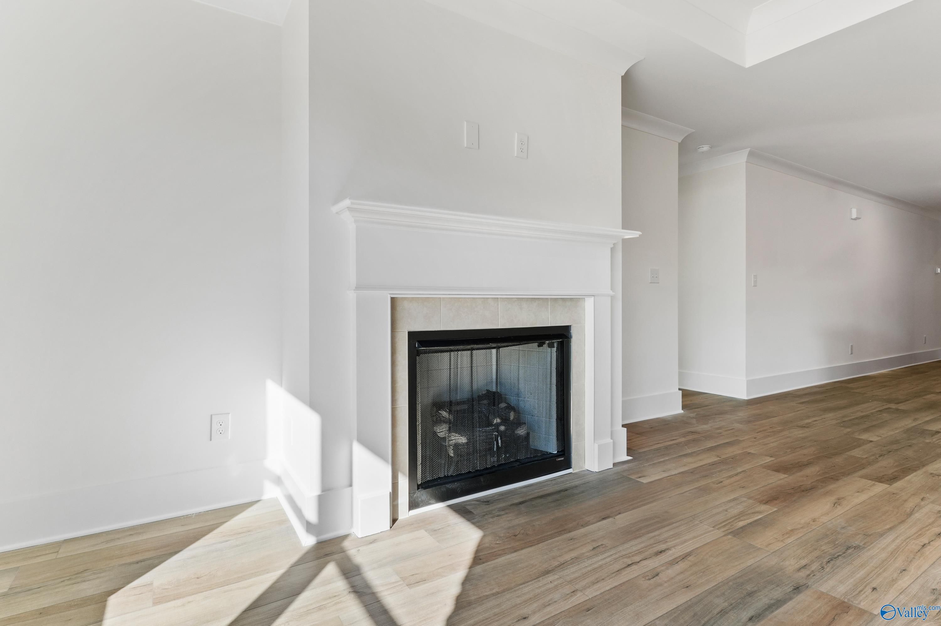 Elegant white mantel gas fireplace with hardwood floors in open living room of The Daphne C 4-bedroom home by Davidson Homes, Arab, Alabama
