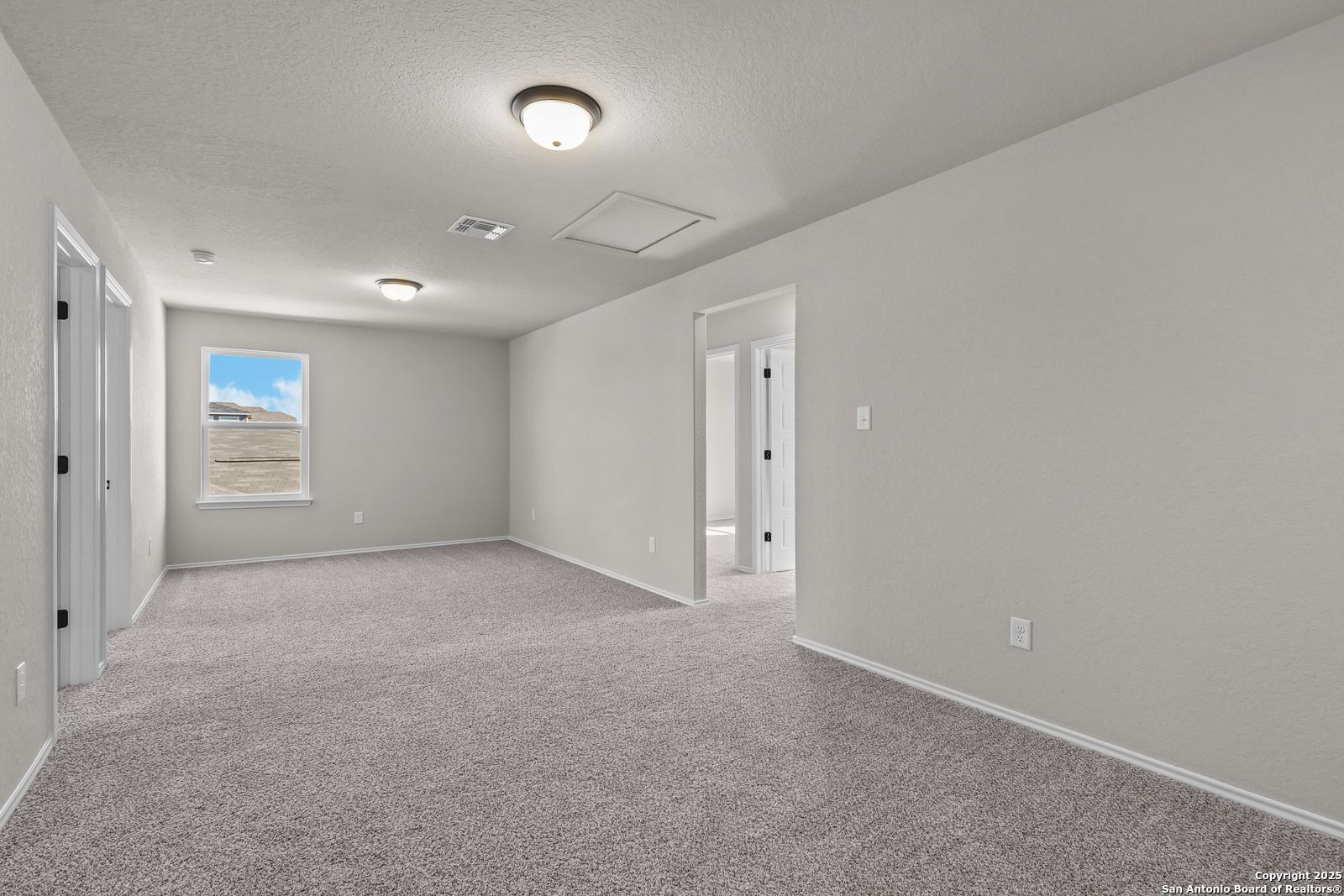 Spacious upstairs bonus room with gray carpet, neutral walls, multiple doorways, and natural light in 5-bedroom The Brazos C home, San Antonio